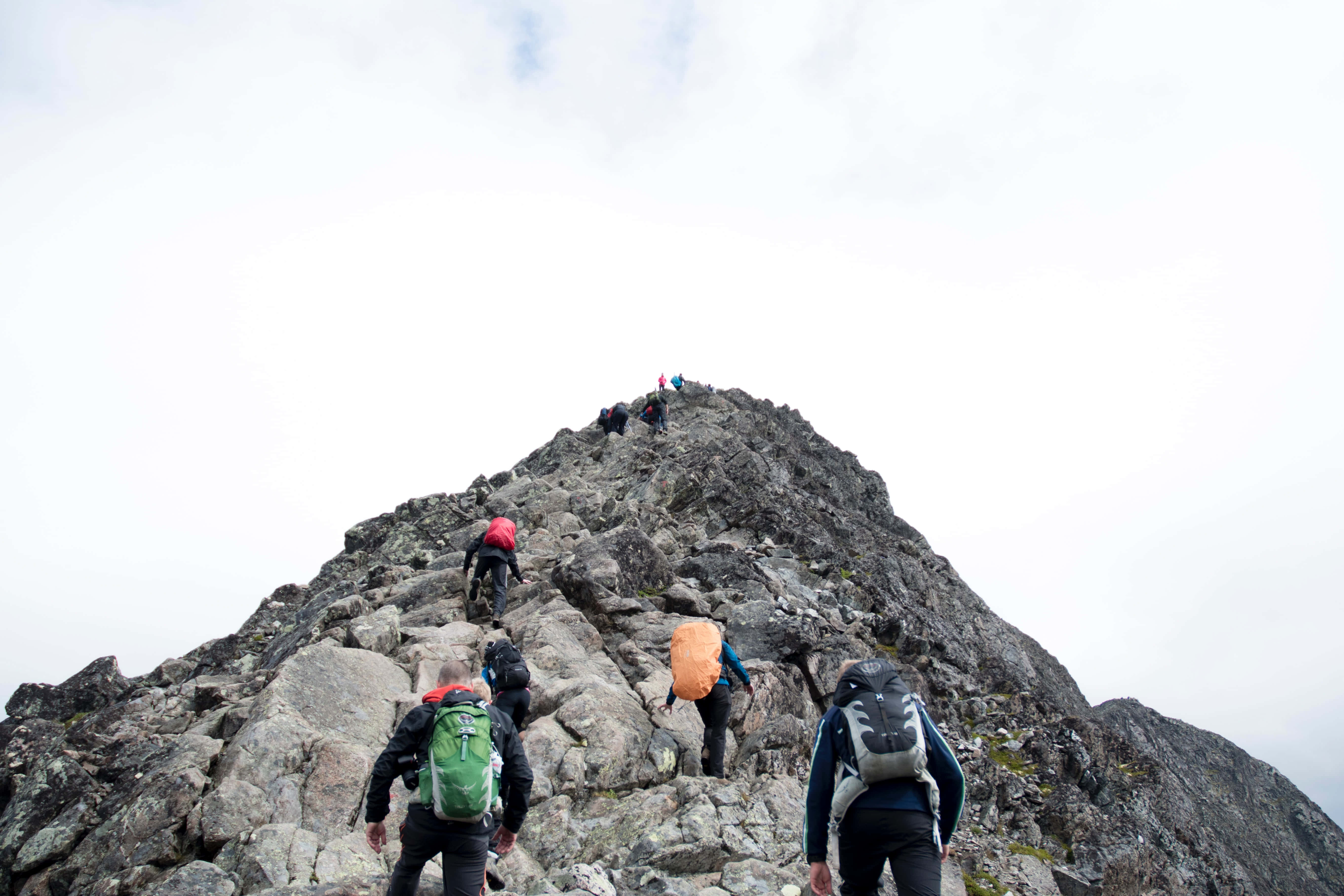 Hiking 桌布 壁紙 — 背著色彩繽紛背包的登山者，在陰天之下攀登崎嶇的岩石山峰。