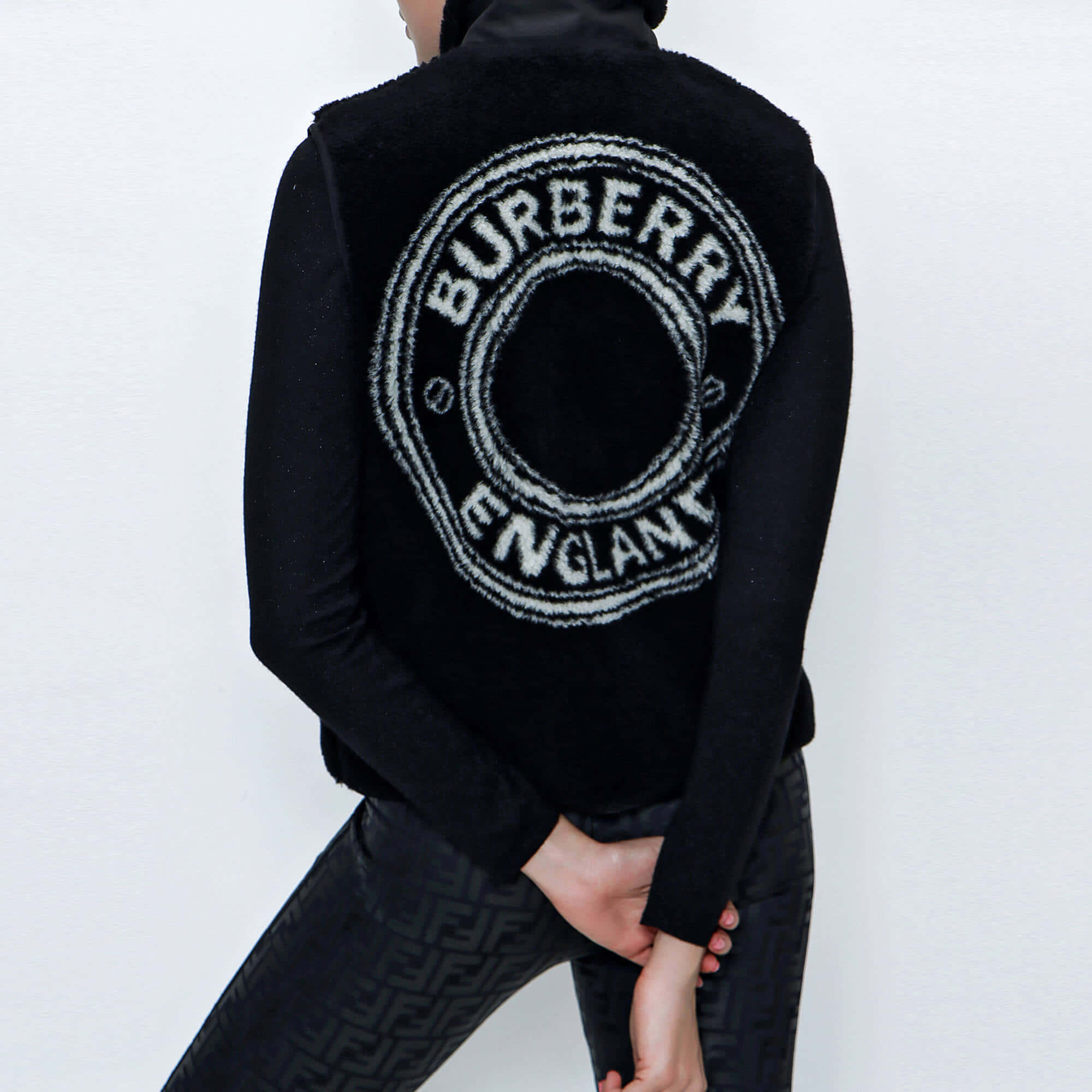 Burberry 桌布 壁紙 — 背面視角，一個人穿著黑色Burberry背心，帶有白色圓形標誌，背景是純白牆壁。
