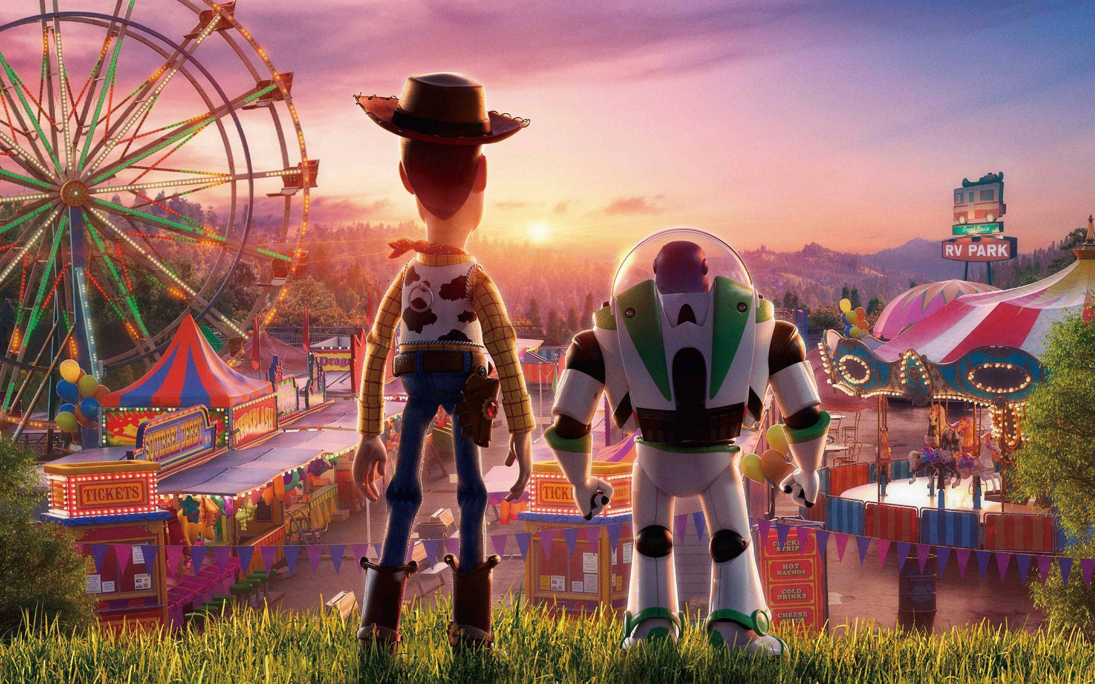 Toy Story 4 桌布 壁紙 — 胡迪和巴斯光年站在草地上，俯瞰著日落時分充滿活力的嘉年華，有巨大的摩天輪和色彩繽紛的遊樂設施。