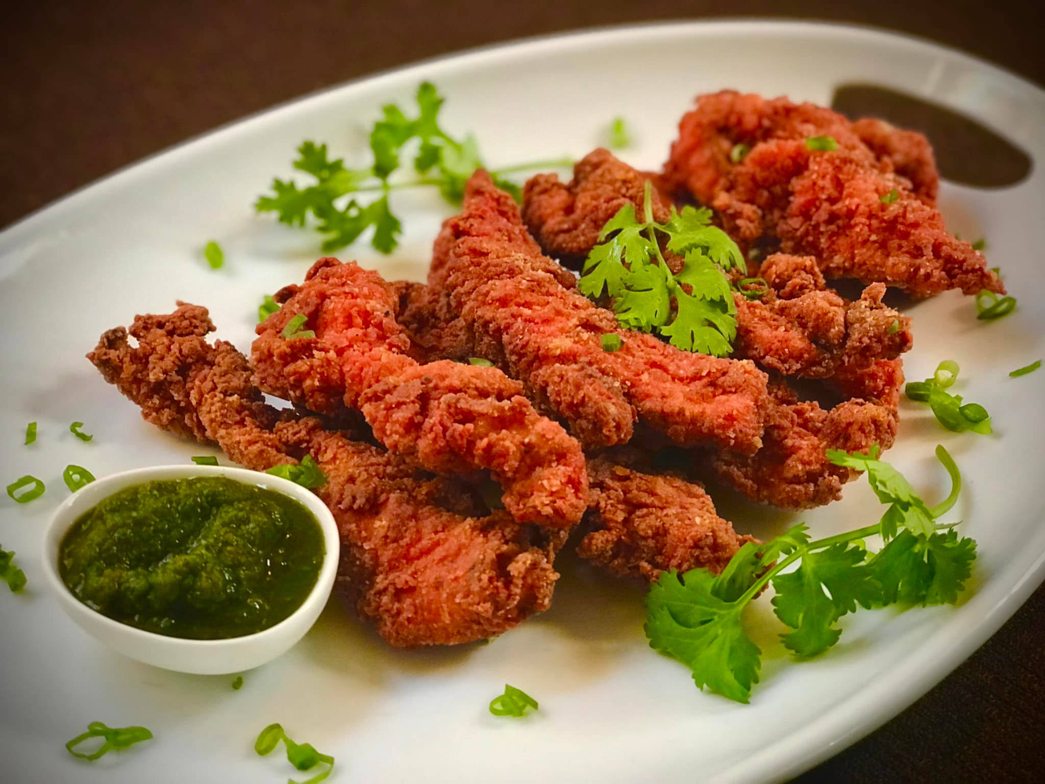 fried chicken 桌布 壁紙 — 脆炸雞柳高高堆在白色盤子上，配上新鮮香菜和綠色醬汁。