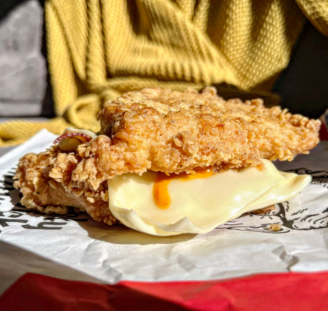 肯德基 桌布 壁紙 — 脆炸雞肉三明治配融化起司和醬汁，放在品牌紙上，背景為黃色針織毛衣。