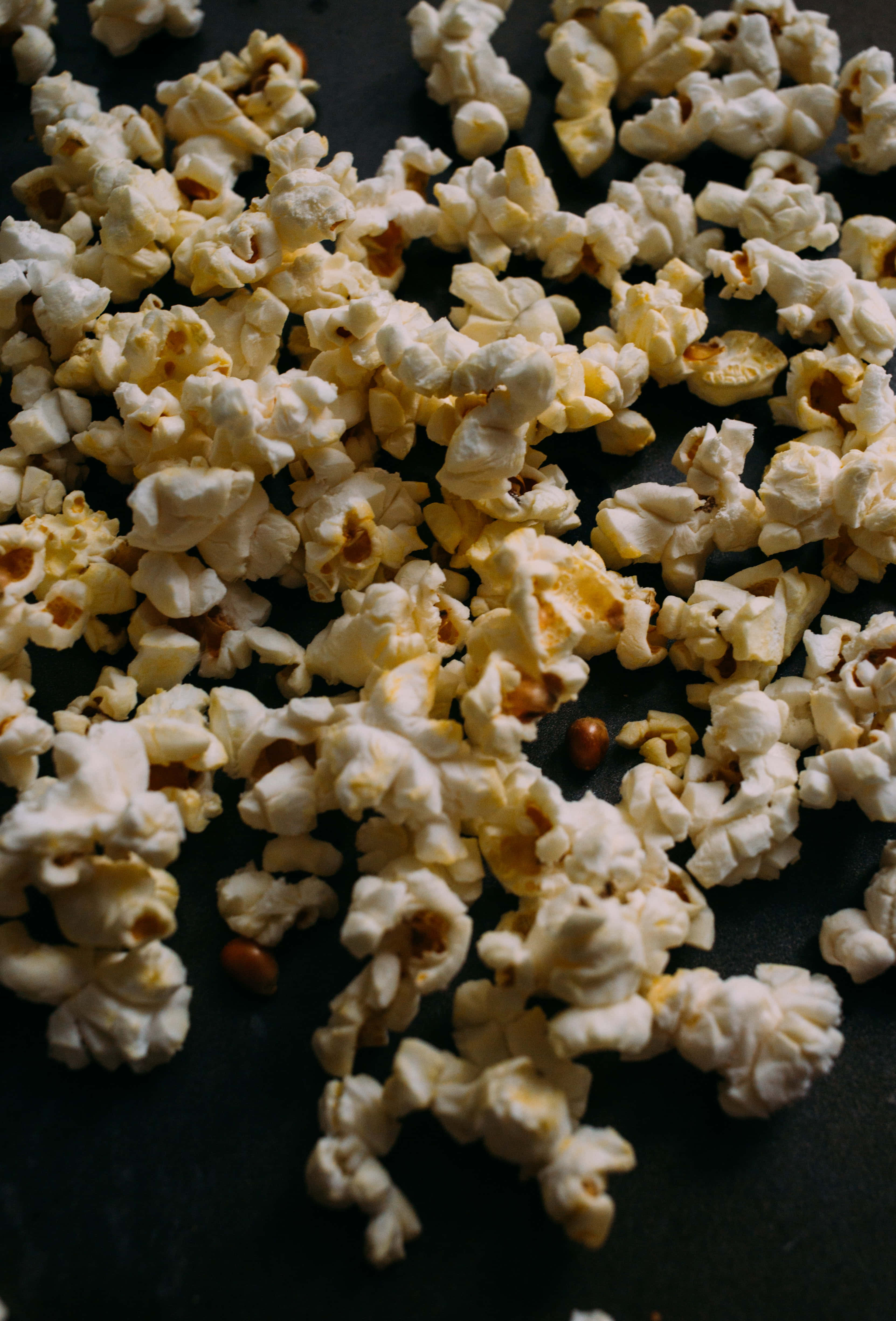 Popcorn 桌布 壁紙 — 脆白爆米花粒帶有金黃色斑點，散落在深色表面上。