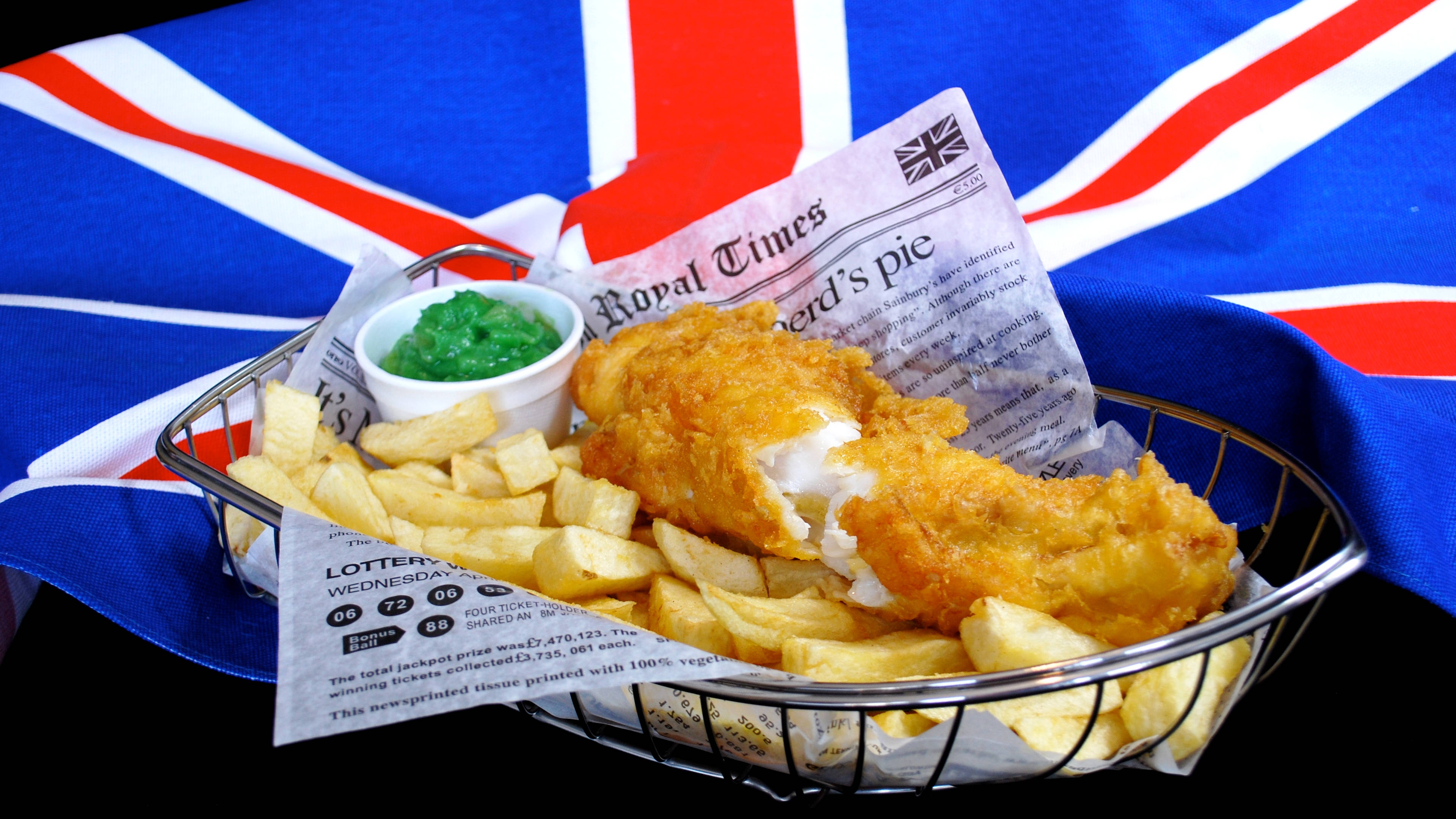 England Flag 桌布 壁紙 — 脆皮炸魚薯條放在鐵絲籃中，置於報紙上，背景為英國國旗。
