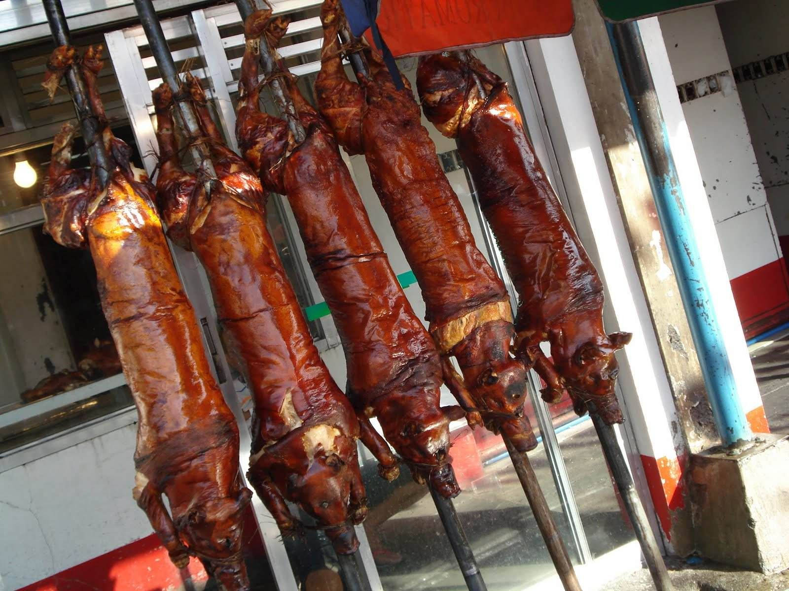 Pig 桌布 壁紙 — 脆皮烤全豬在繁忙的路邊攤外閃閃發光地掛在烤叉上。