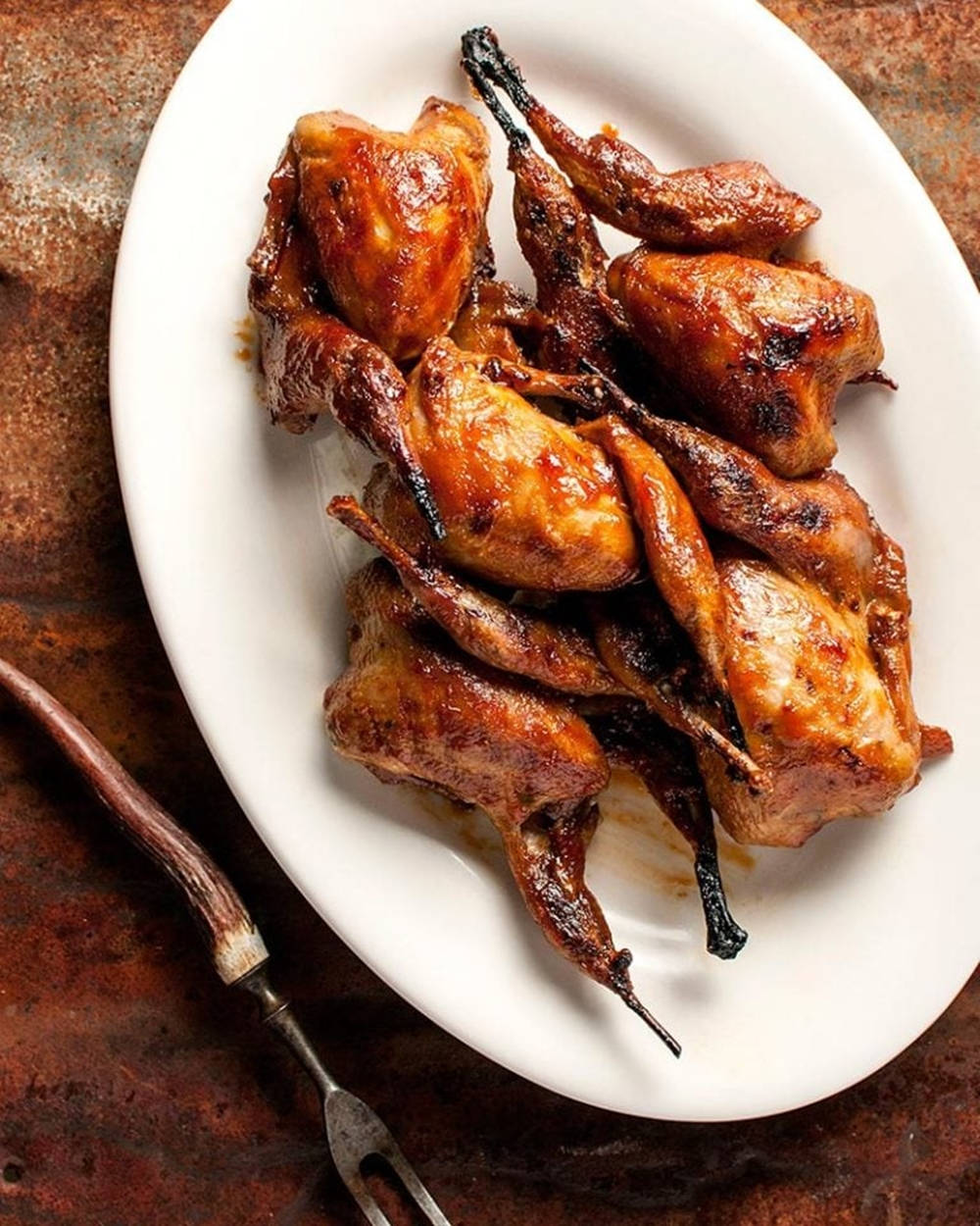 Quail 桌布 壁紙 — 脆皮烤鵪鶉配焦糖釉，高高堆在白色橢圓形盤子上，背景是質樸的鏽蝕金屬。