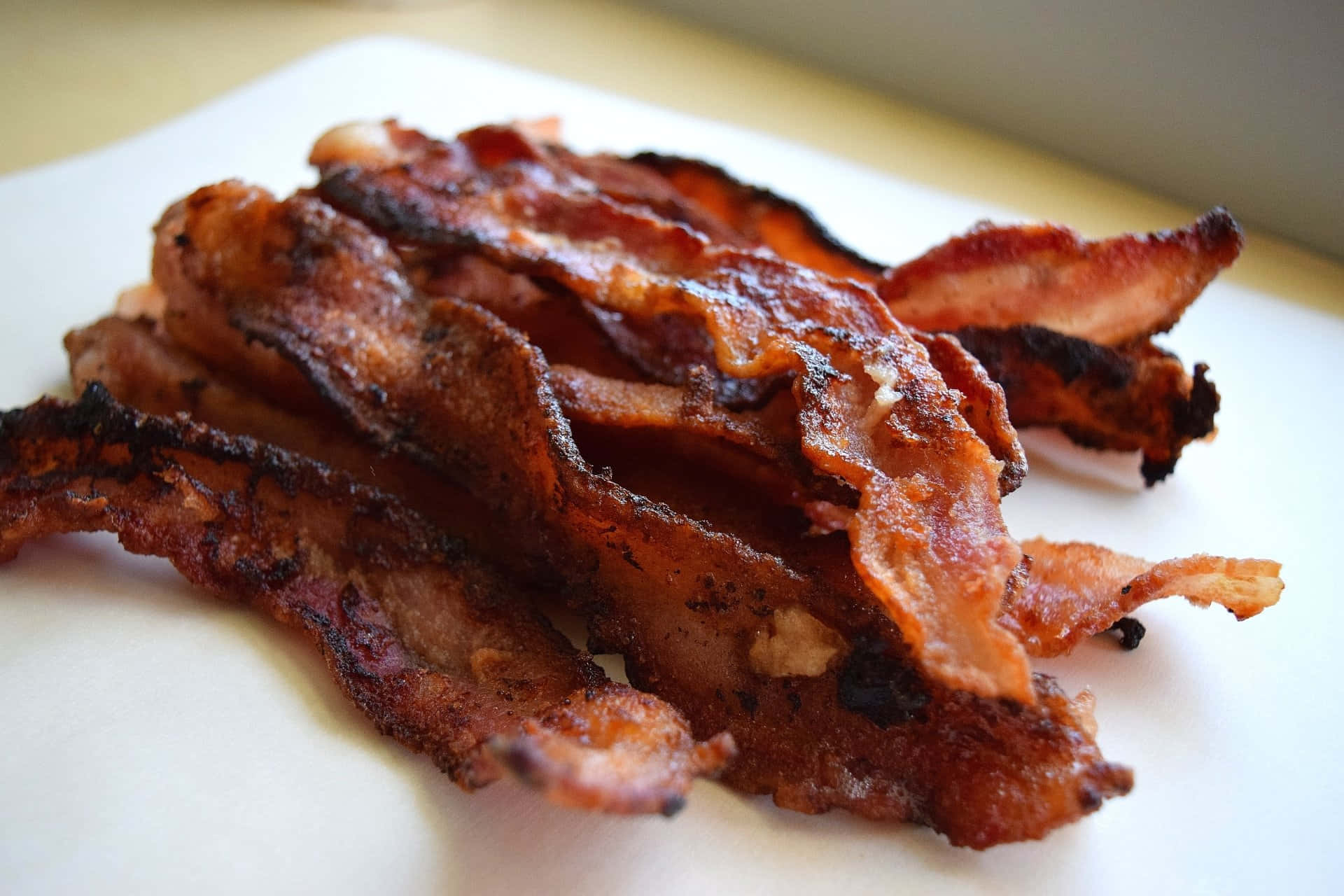 bacon 桌布 壁紙 — 脆皮金黃色培根條在白色盤子上閃爍著融化的油脂。