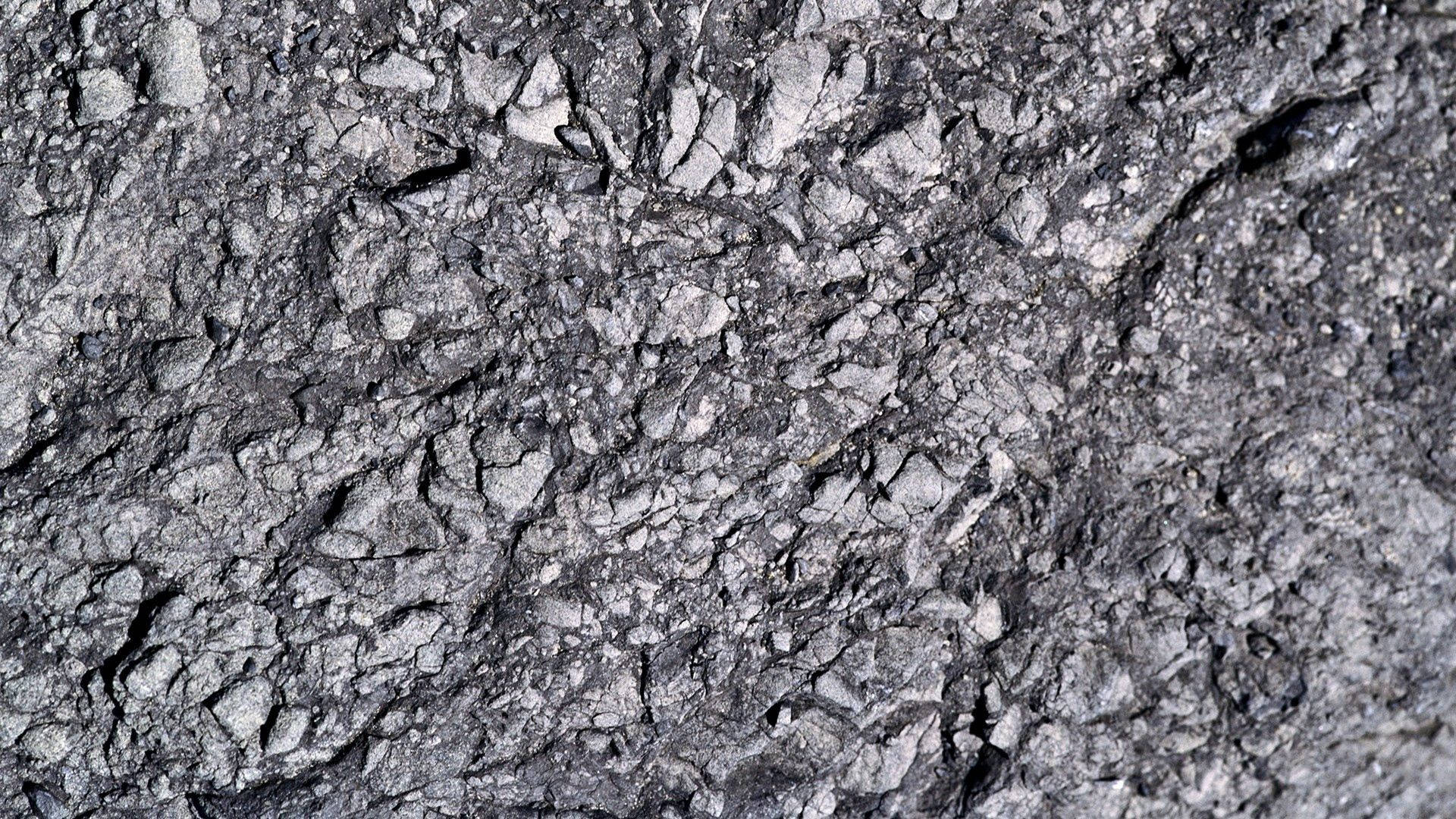 Stone 桌布 壁紙 — 自然光下裂開的瀝青路面、碎裂灰色石頭和深裂縫的特寫。