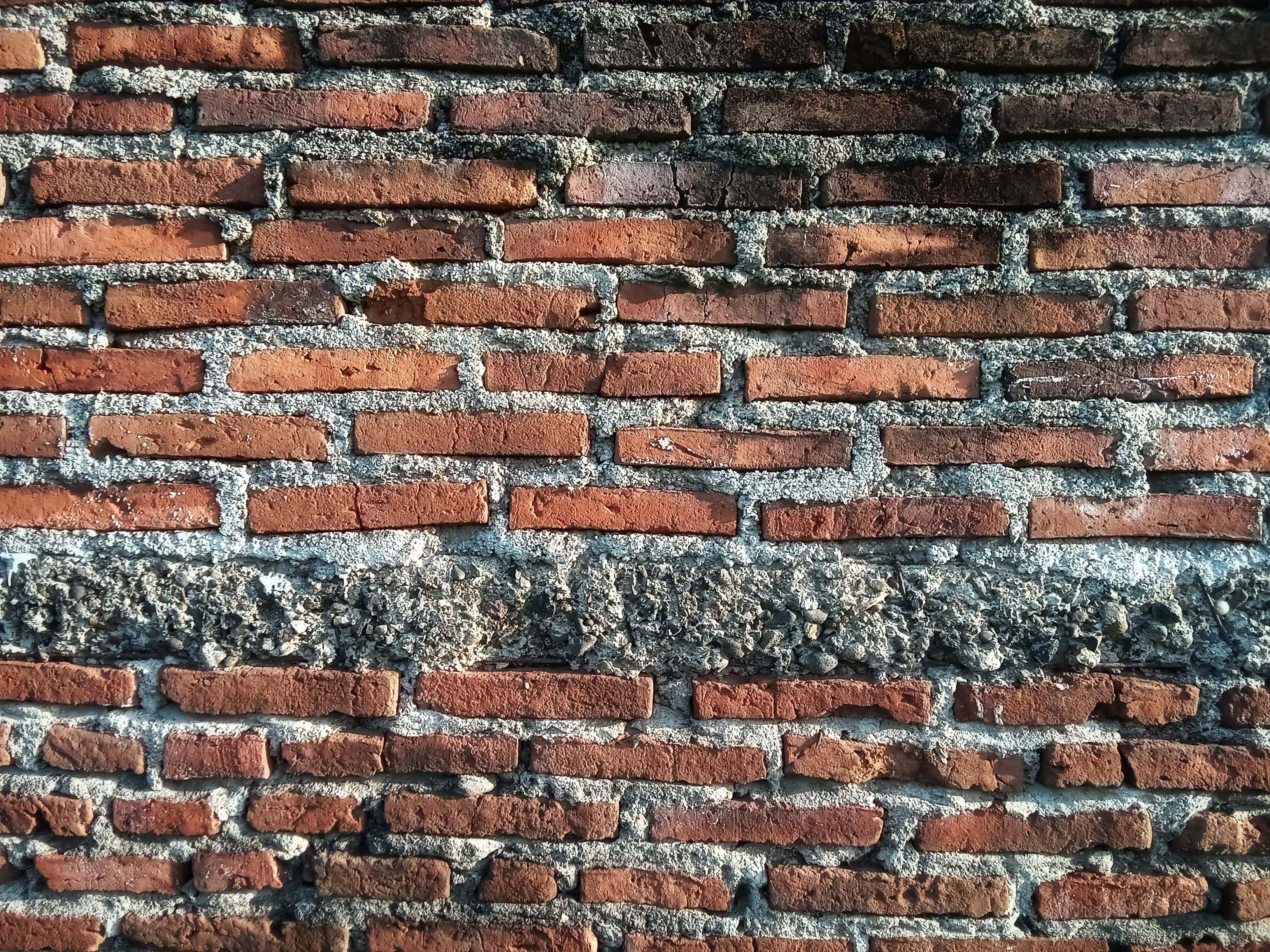 Brick Wall 桌布 壁紙 — 自然光下風化紅磚牆的特寫，帶有灰色砂漿和可見紋理。