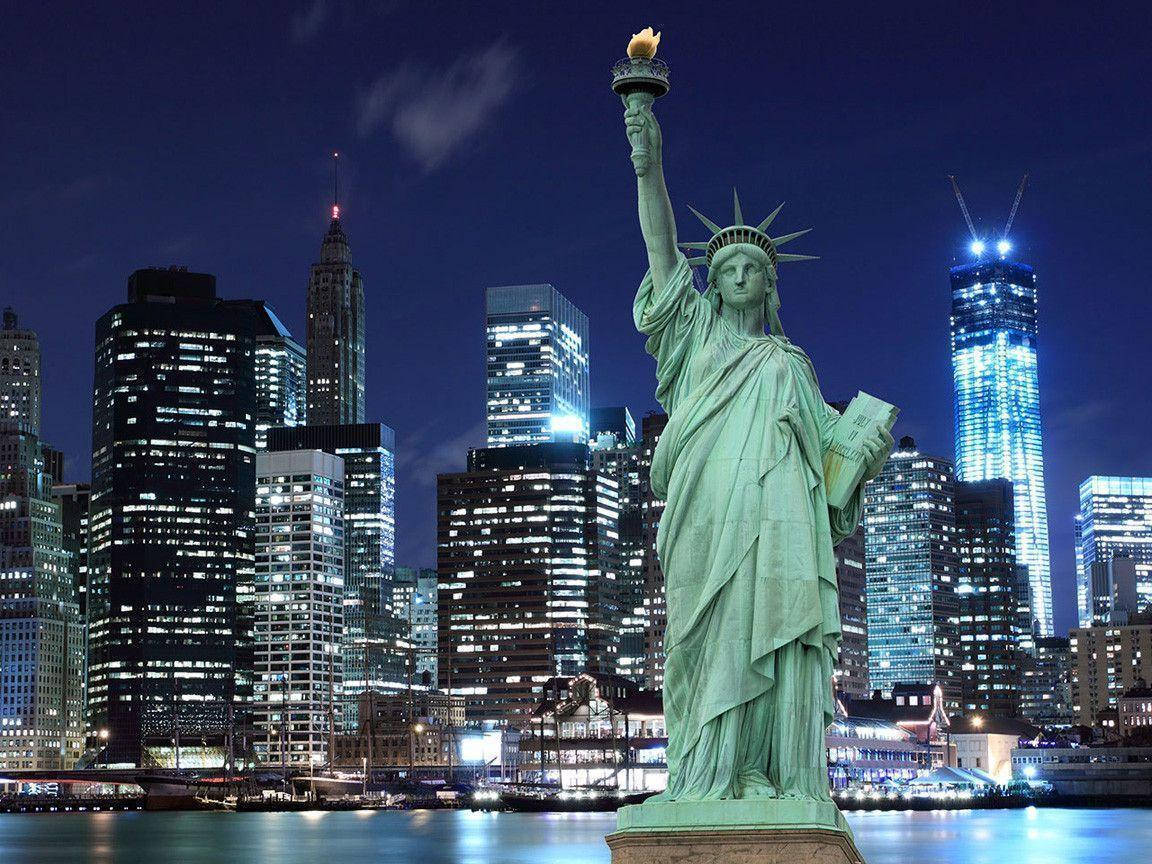 New York 桌布 壁紙 — 自由女神像在充滿活力的夜空下巍然聳立，發光的摩天大樓倒映在水面上。