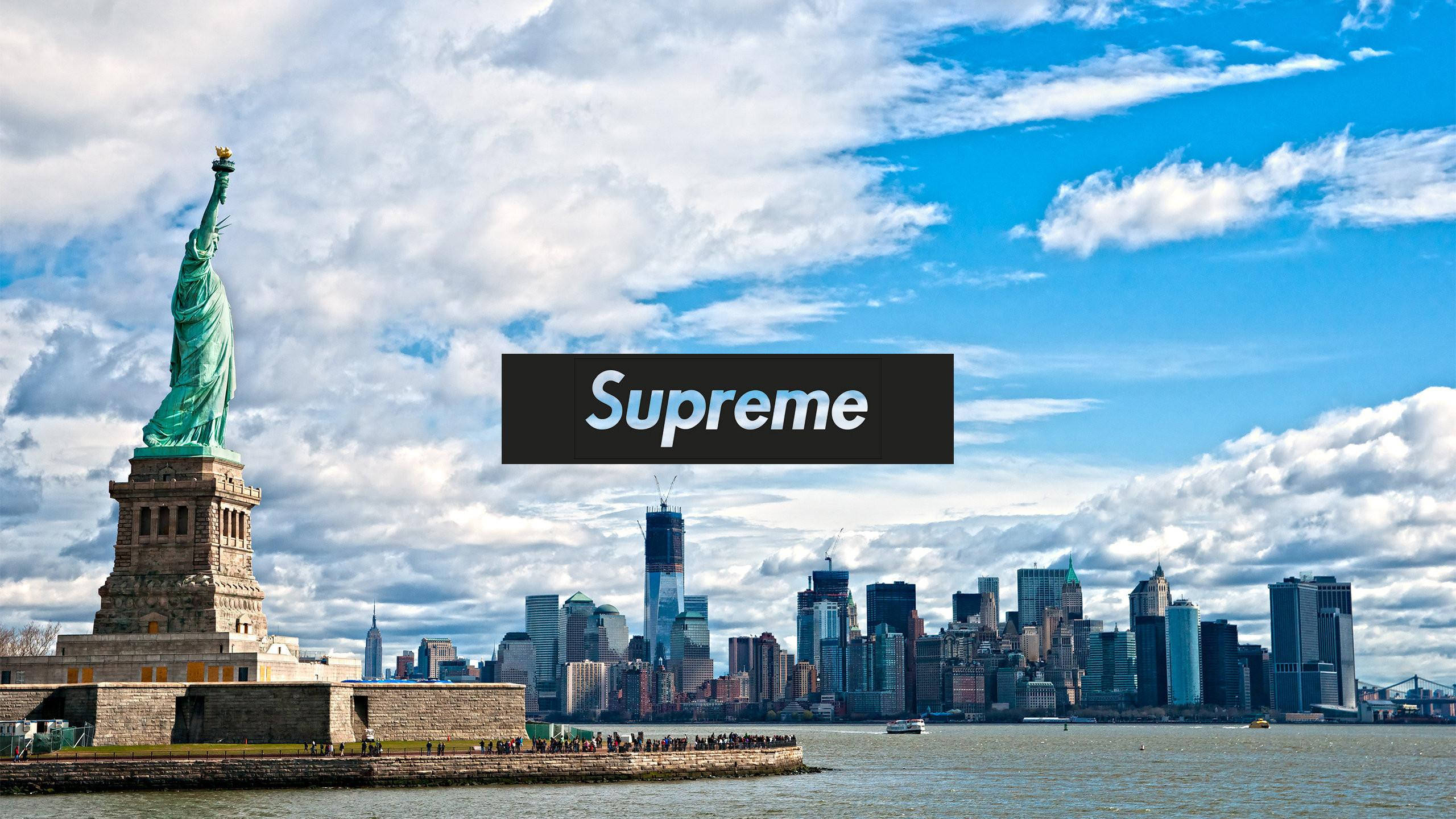 Cool Supreme 桌布 壁紙 — 自由女神像在明亮的藍天和蓬鬆的白雲下，高聳於紐約市天際線旁。