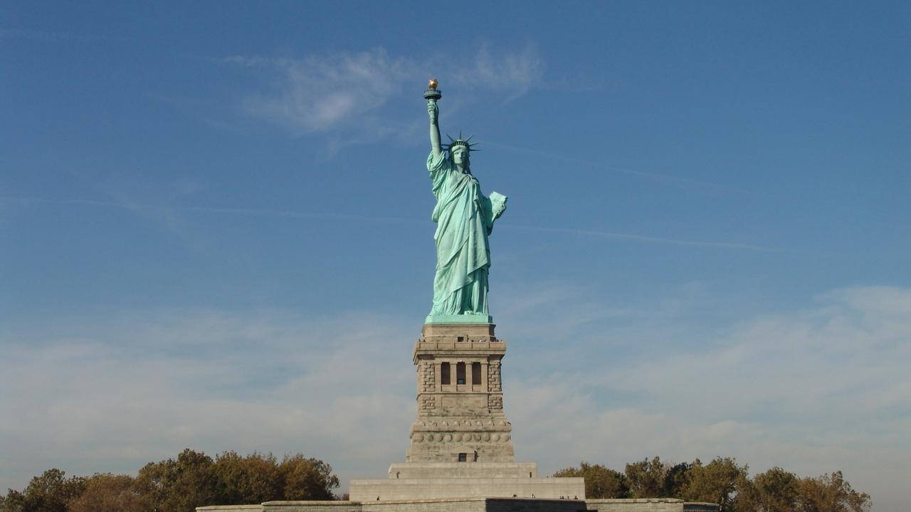 New York 桌布 壁紙 — 自由女神像在晴朗的藍天下高高聳立，伴隨著縷縷白雲和底部的秋樹。
