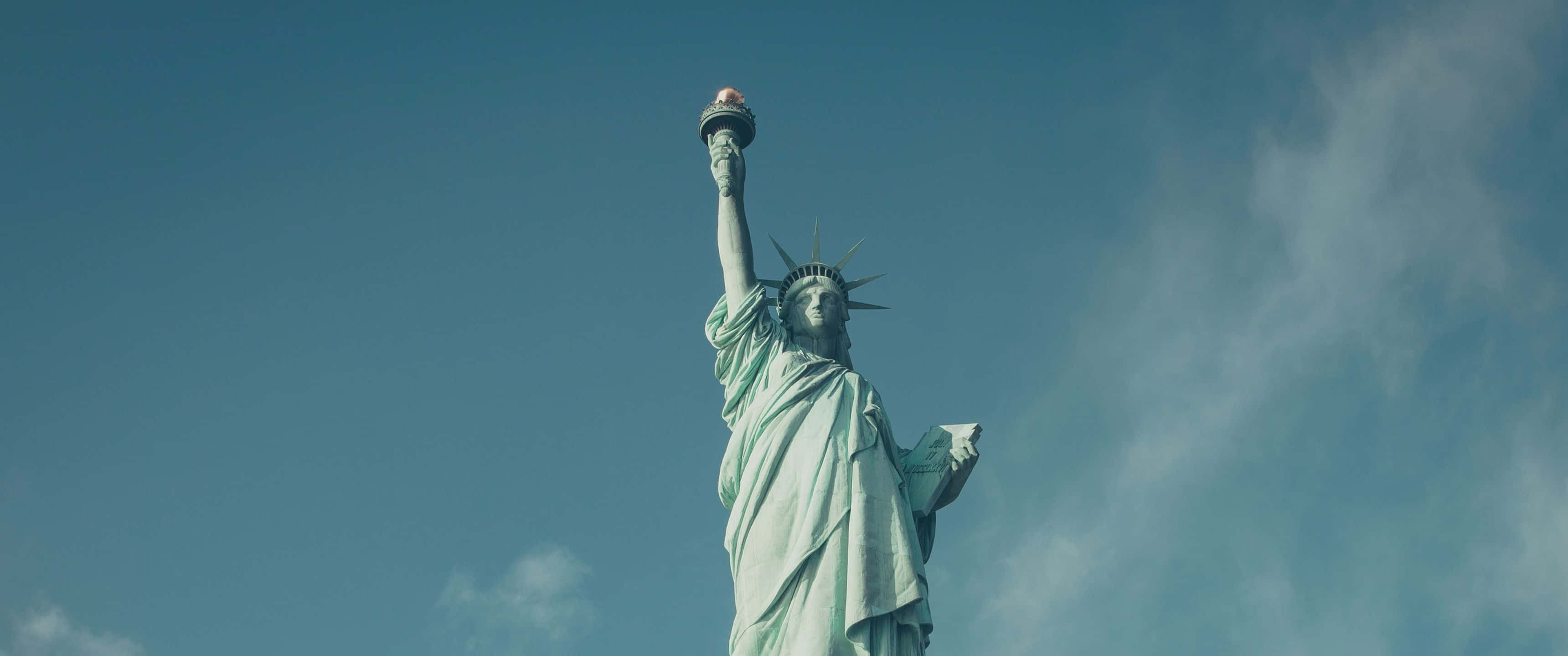 Statue Of Liberty 桌布 壁紙 — 自由女神像在晴朗藍天和縷縷白雲的襯托下高高聳立，高舉火炬。
