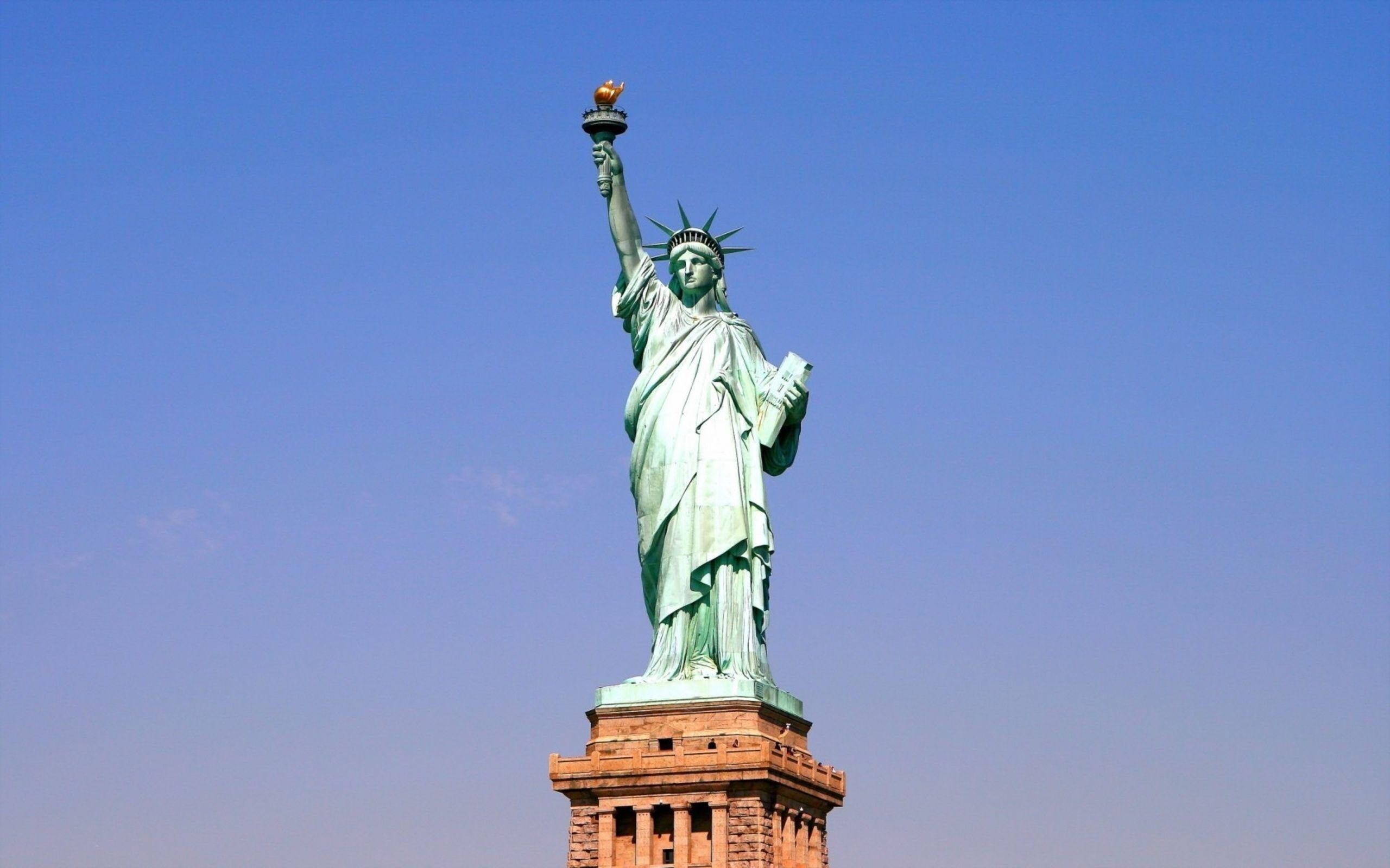 New York 桌布 壁紙 — 自由女神像在清澈的藍天下高高聳立，高舉火炬，低持石板。