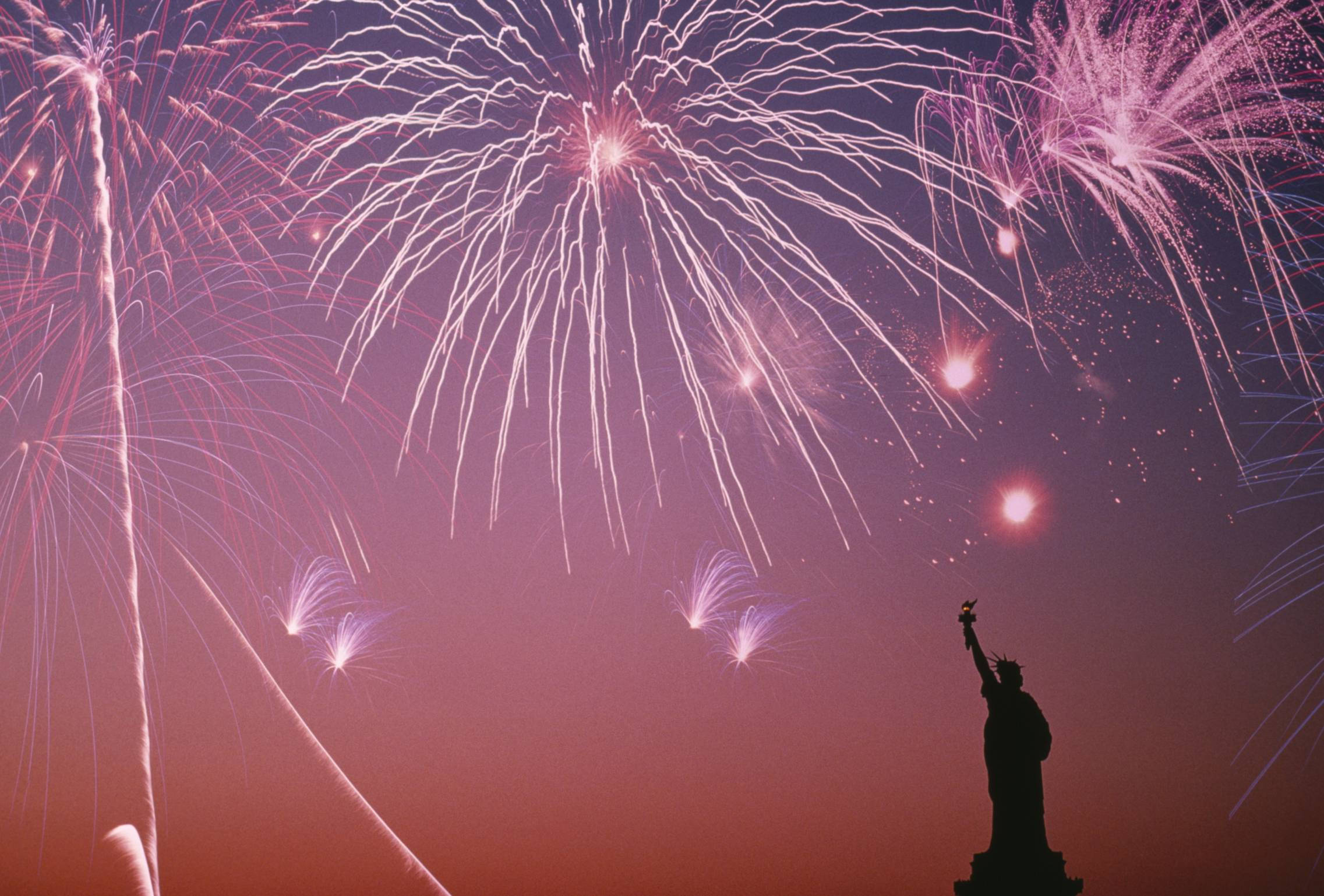 fourth of july 桌布 壁紙 — 自由女神像的剪影，背景是暮色天空，綻放著充滿活力的粉紅色和白色煙火。