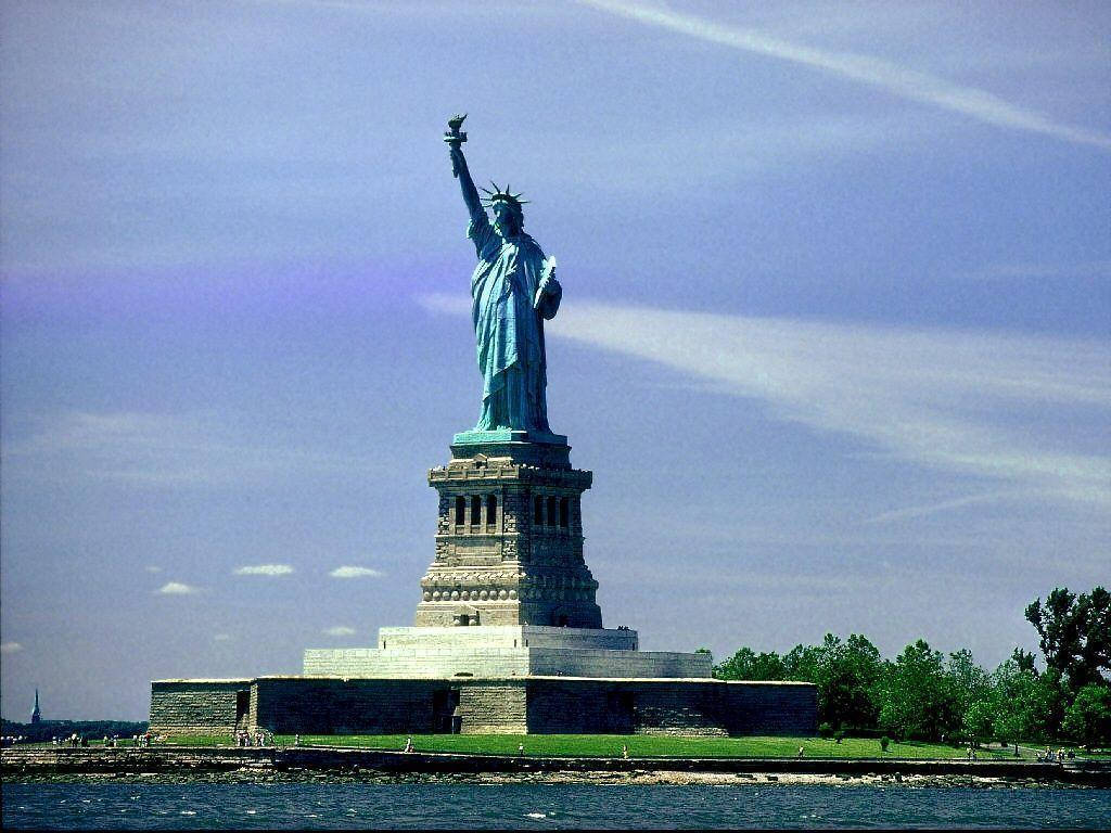 New York 桌布 壁紙 — 自由女神像矗立在自由島上，其標誌性的綠色銅鏽在藍天白雲的映襯下格外醒目。