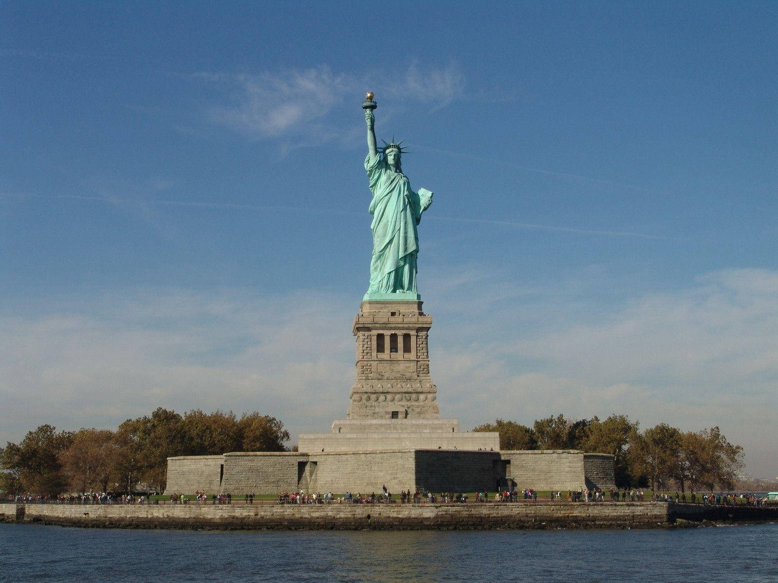 New York 桌布 壁紙 — 自由女神像聳立在自由島上，遊客聚集在其底座周圍，天空晴朗湛藍。