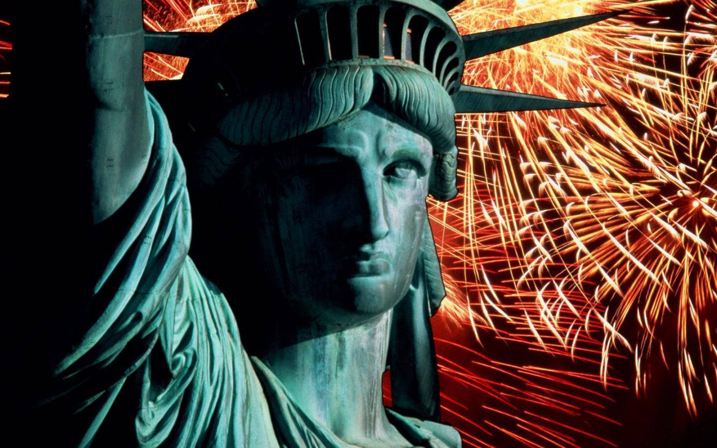 Fireworks 桌布 壁紙 — 自由女神像臉部的特寫，背景是充滿活力的橙色和紅色煙火。