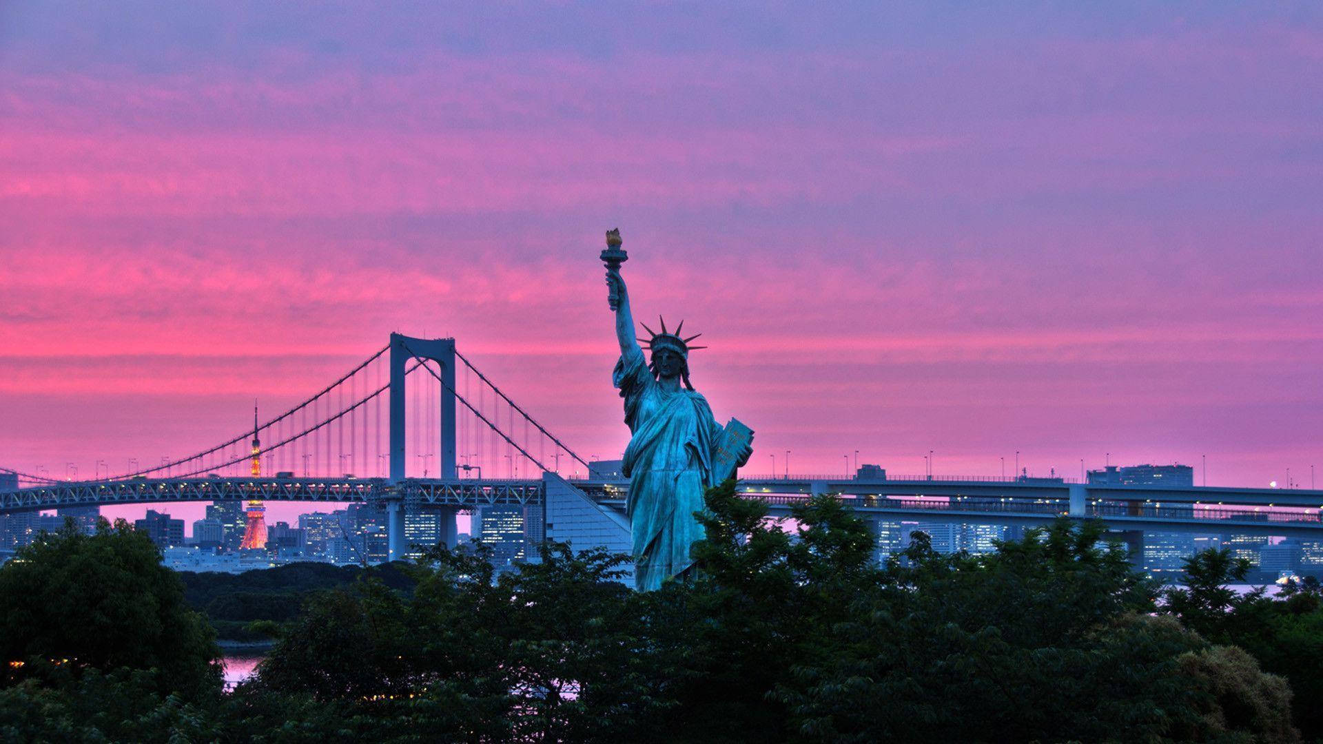 Statue Of Liberty 桌布 壁紙 — 自由女神像複製品在充滿活力的粉紅色和紫色日落天空下高高聳立，背景是彩虹橋和東京天際線。
