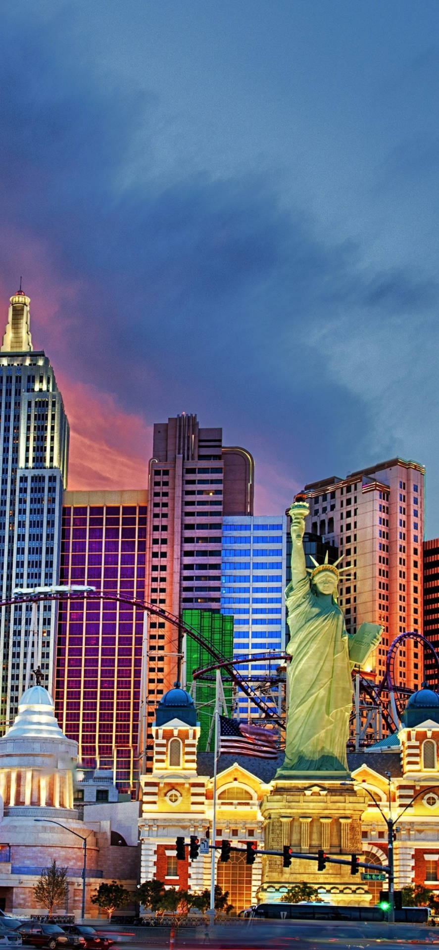 Vegas iPhone 桌布 壁紙 — 自由女神像複製品在拉斯維加斯天際線上方，以充滿活力的暮色天空為背景，聳立發光，周圍是閃爍的摩天大樓。