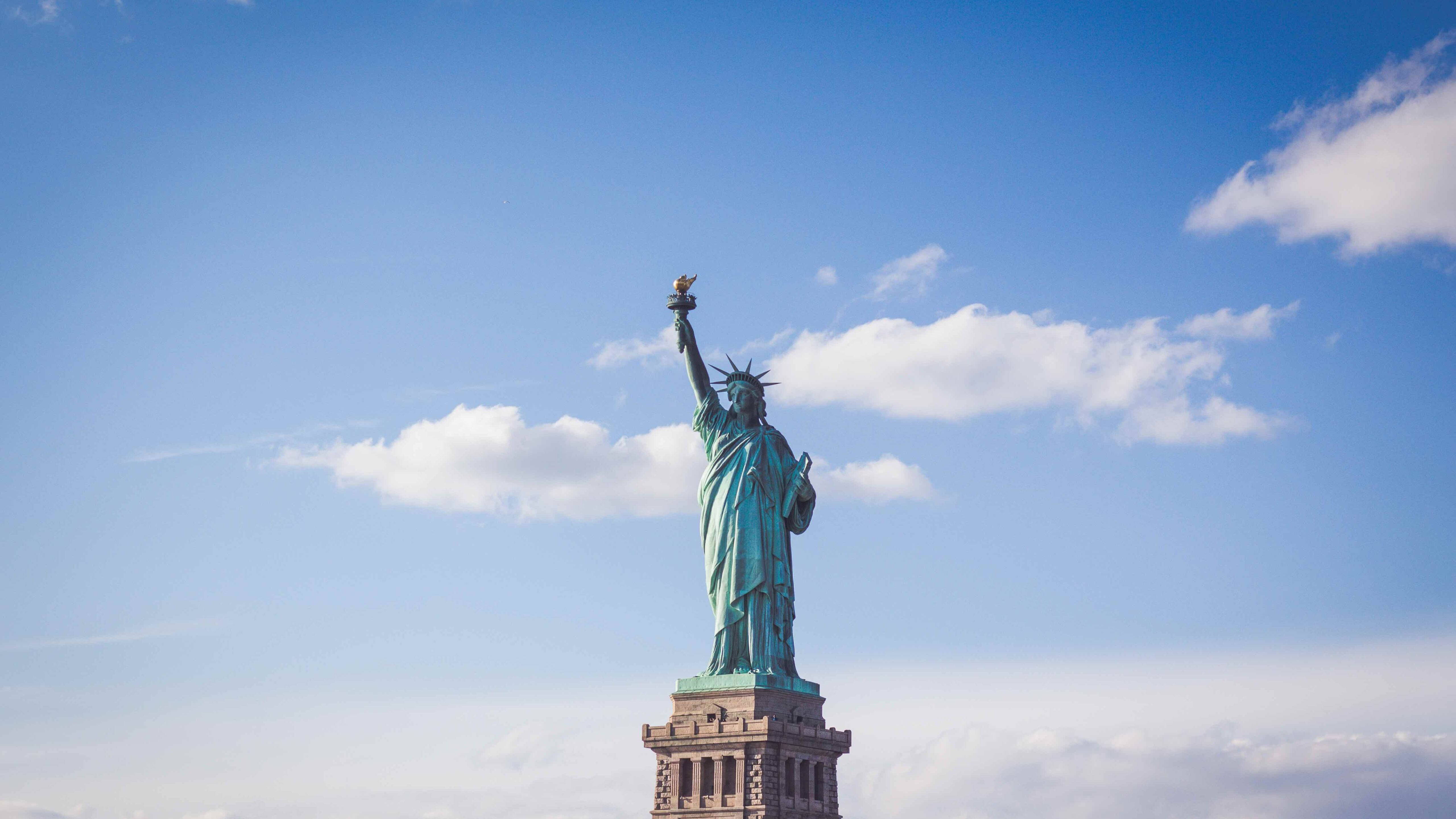 New York 桌布 壁紙 — 自由女神像高聳入雲，在明亮的藍天白雲下高舉火炬。