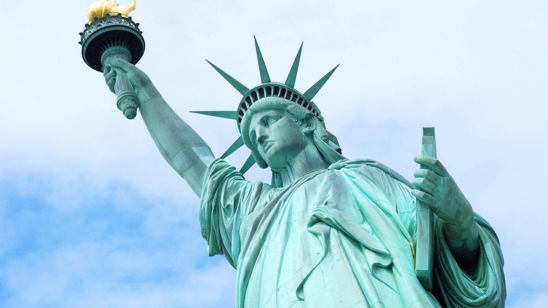 New York 桌布 壁紙 — 自由女神像高聳入雲，部分多雲的天空下，手持火炬和石板。