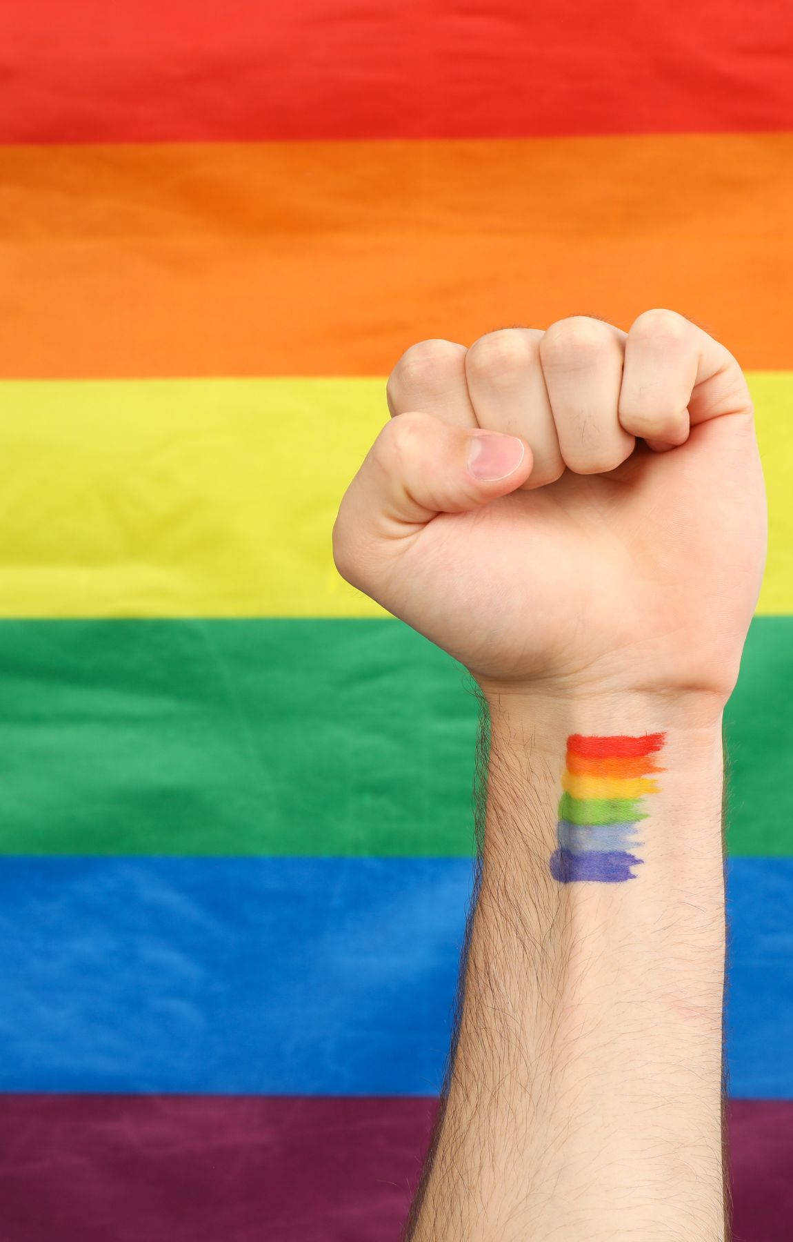 Subtle Lgbt 桌布 壁紙 — 舉起的拳頭，手腕上有彩虹紋身，背景是模糊的彩虹旗。