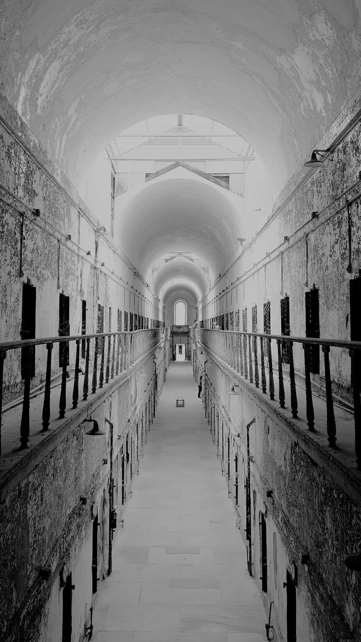 Jail 桌布 壁紙 — 舊監獄中一條長長的黑白走廊，拱形天花板，兩側排列著牢房門。