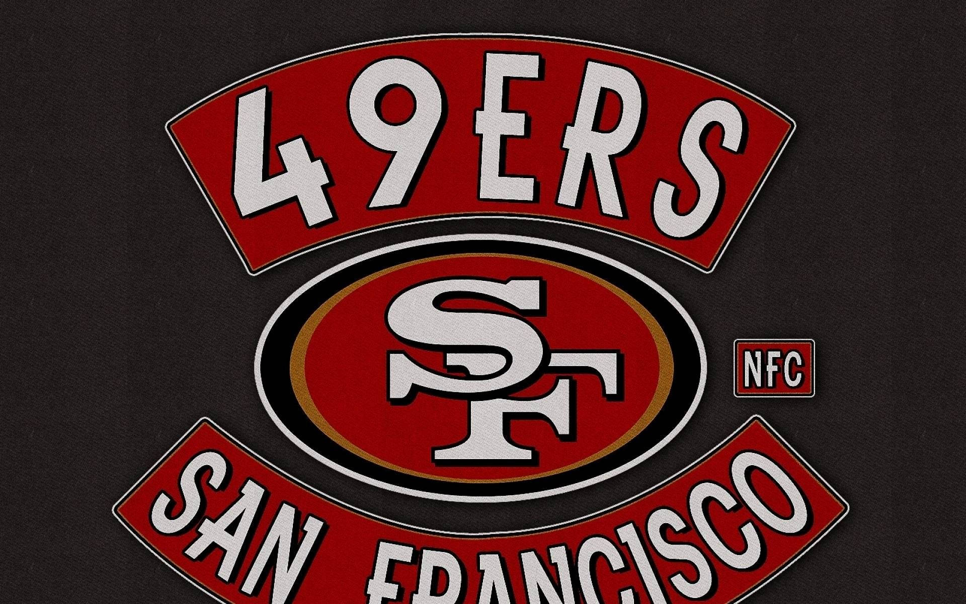 49ers 桌布 壁紙 — 舊金山49人NFL球隊標誌近距離特寫，以紅、白、金色繡在黑色布料上。