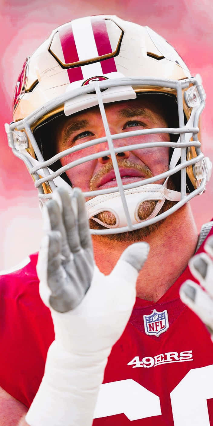 Mike Mcglinchey 桌布 壁紙 — 舊金山49人美式足球員身穿紅色球衣及頭盔，在柔和粉紅色背景前向球迷揮手的特寫。