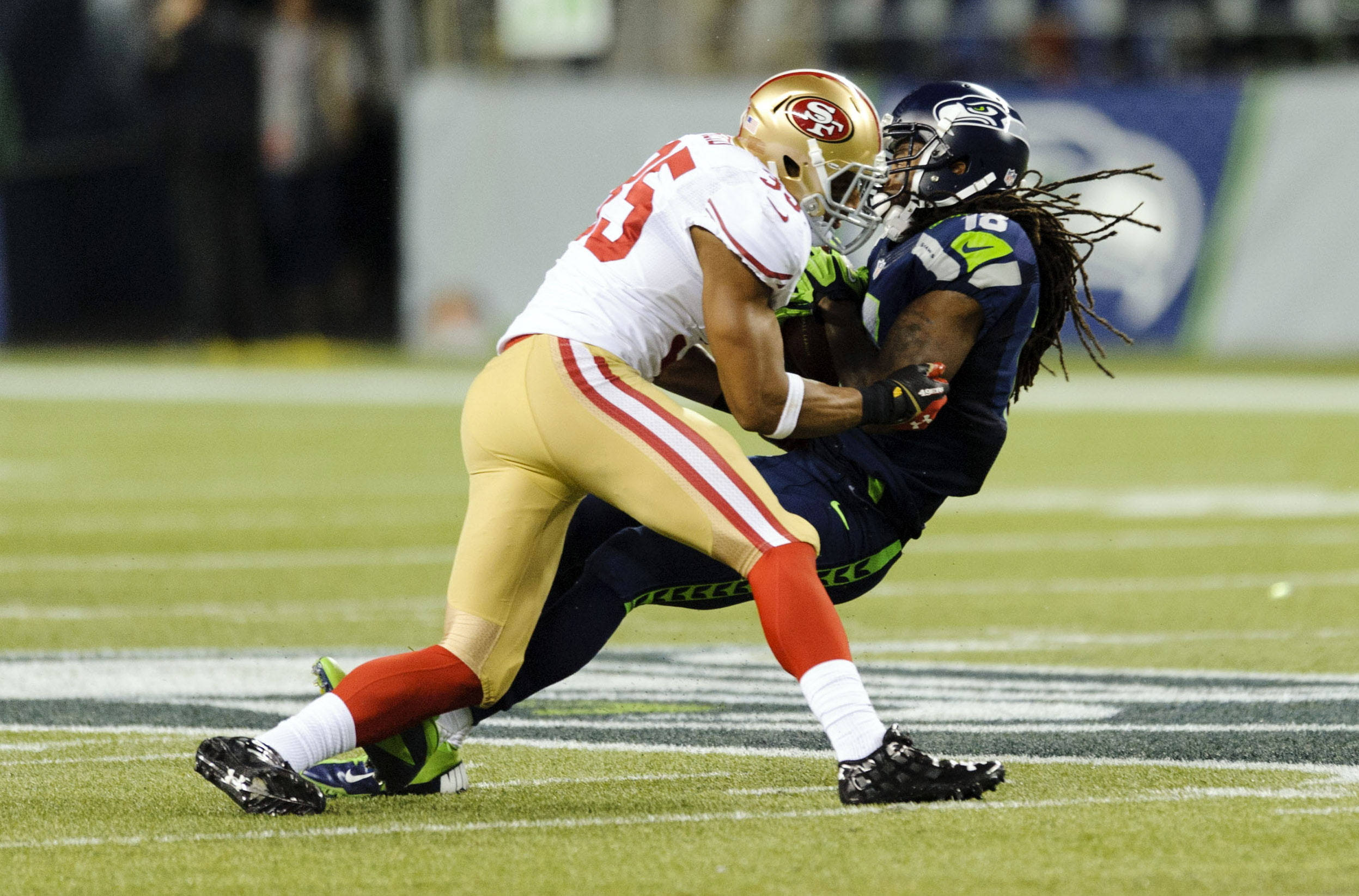 Seattle Seahawks 桌布 壁紙 — 舊金山49人隊的防守球員在充滿活力的綠色足球場上，於比賽中擒抱西雅圖海鷹隊的球員。