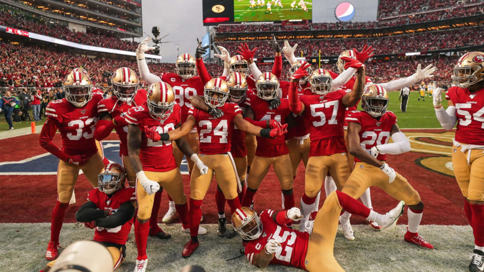 49ers 桌布 壁紙 — 舊金山49人隊美式足球員身穿紅色和金色球衣，在球場上高舉雙臂，頭盔在體育場燈光下閃閃發光，勝利慶祝。
