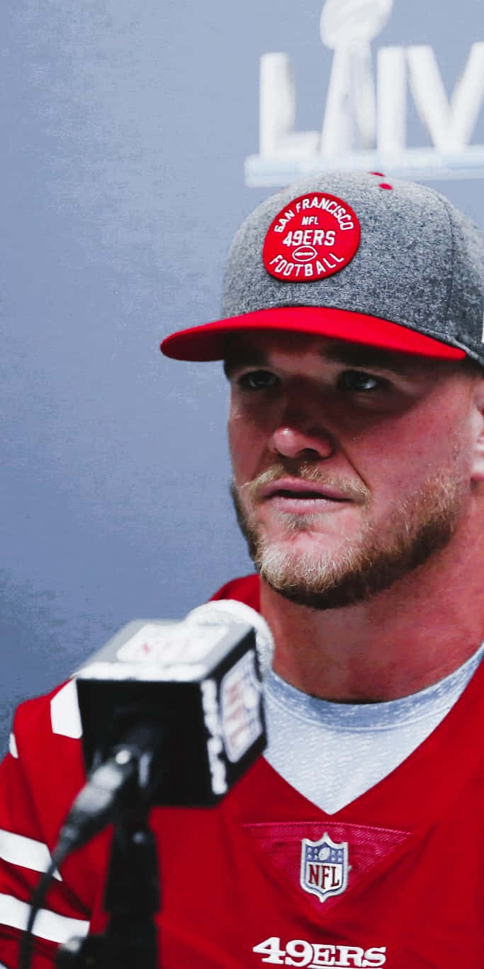 Mike Mcglinchey 桌布 壁紙 — 舊金山四九人美式足球員近照，身穿球隊帽和球衣，在記者會上使用麥克風。