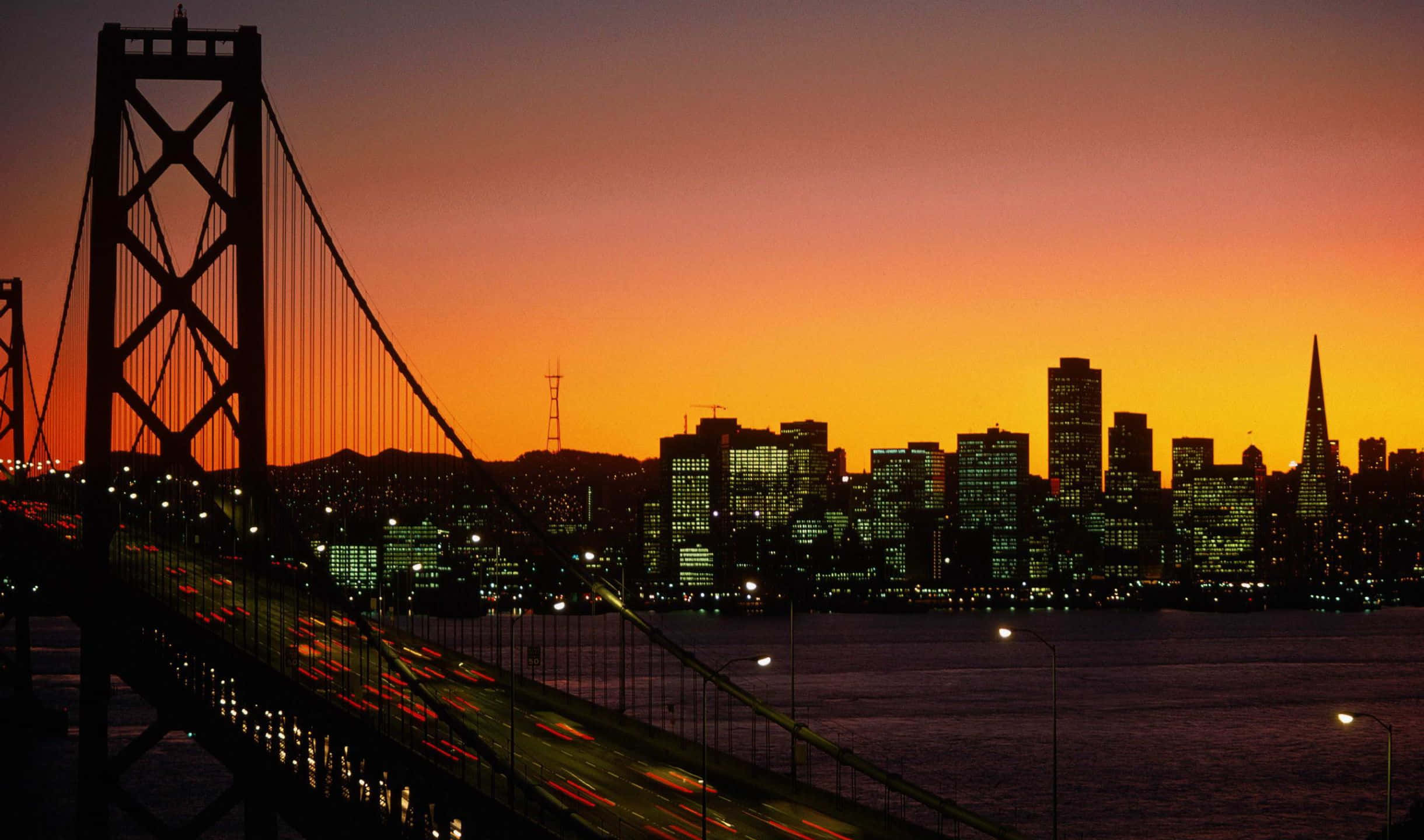 2440x1440 San Francisco 桌布 壁紙 — 舊金山天際線在日落時分，海灣大橋在熾熱的橙色和粉紅色天空下形成剪影。