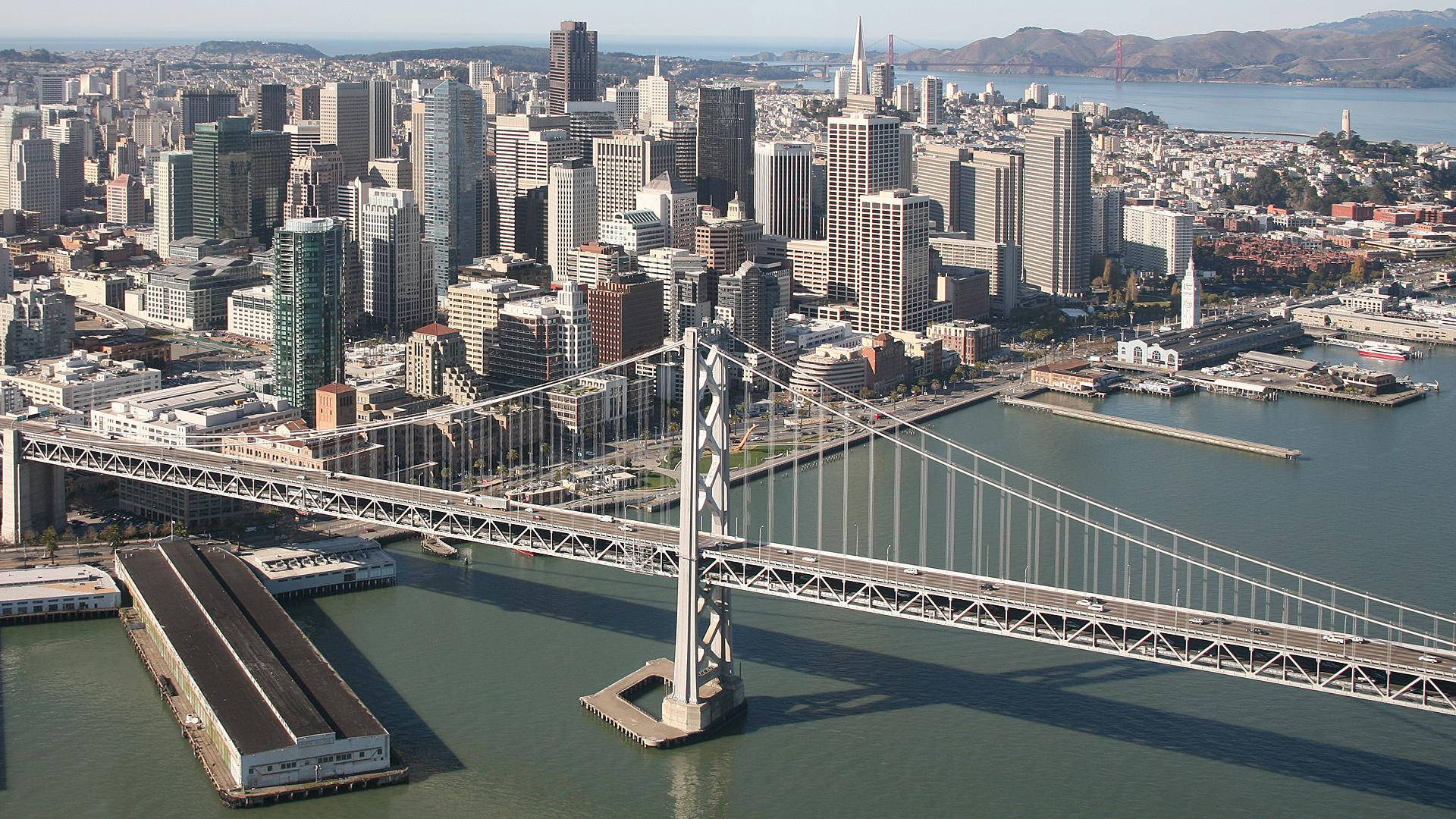 San Francisco HD 桌布 壁紙 — 舊金山天際線的鳥瞰圖，海灣大橋橫跨碧綠海水，城市摩天大樓在清澈藍天下。