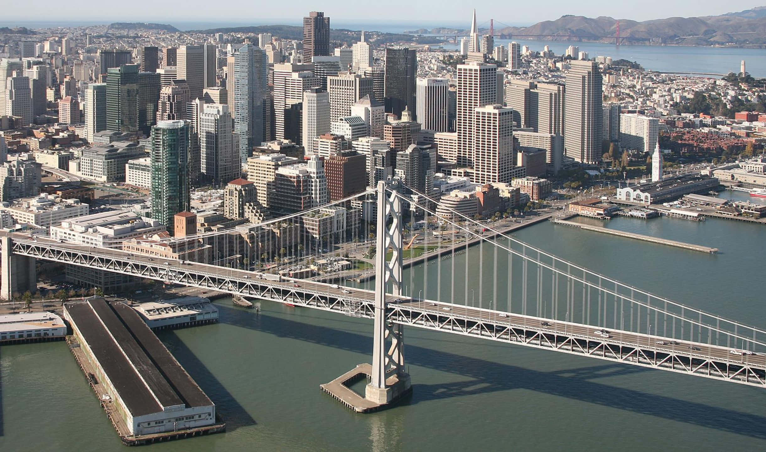 2440x1440 San Francisco 桌布 壁紙 — 舊金山天際線的鳥瞰圖，海灣大橋橫跨水面，城市摩天大樓在晴朗的日光下清晰可見。