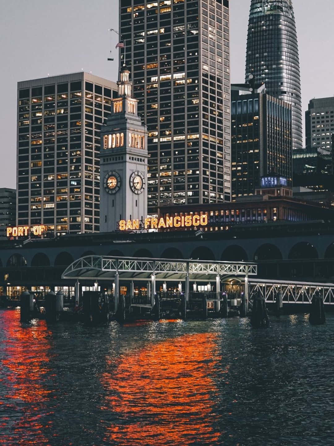 san francisco iPhone 桌布 壁紙 — 舊金山海濱在黃昏時分，水面泛起橙色光芒，城市高樓聳立。