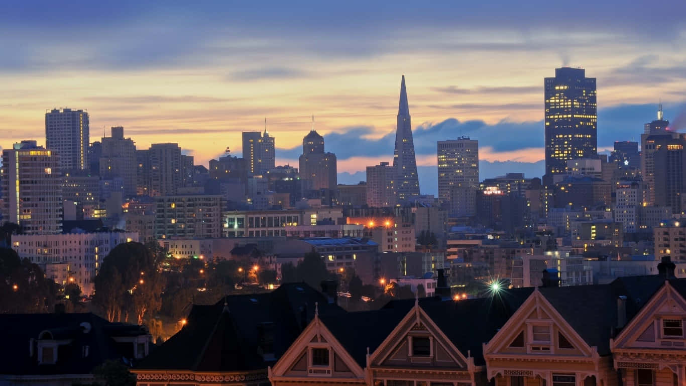 1366x768 San Francisco 桌布 壁紙 — 舊金山黃昏時分天際線，建築物和前景的維多利亞式房屋閃爍著金色燈光。