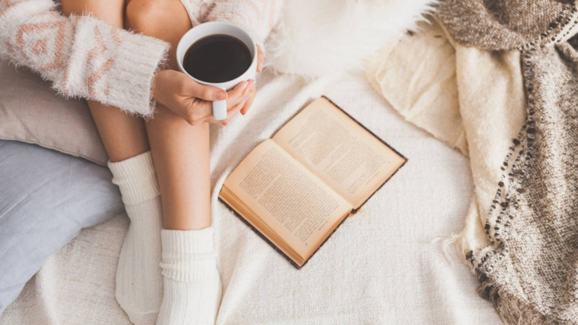 Reading 桌布 壁紙 — 舒適的人穿著毛絨毛衣，在柔軟的毯子上拿著咖啡杯，旁邊放著一本打開的書。