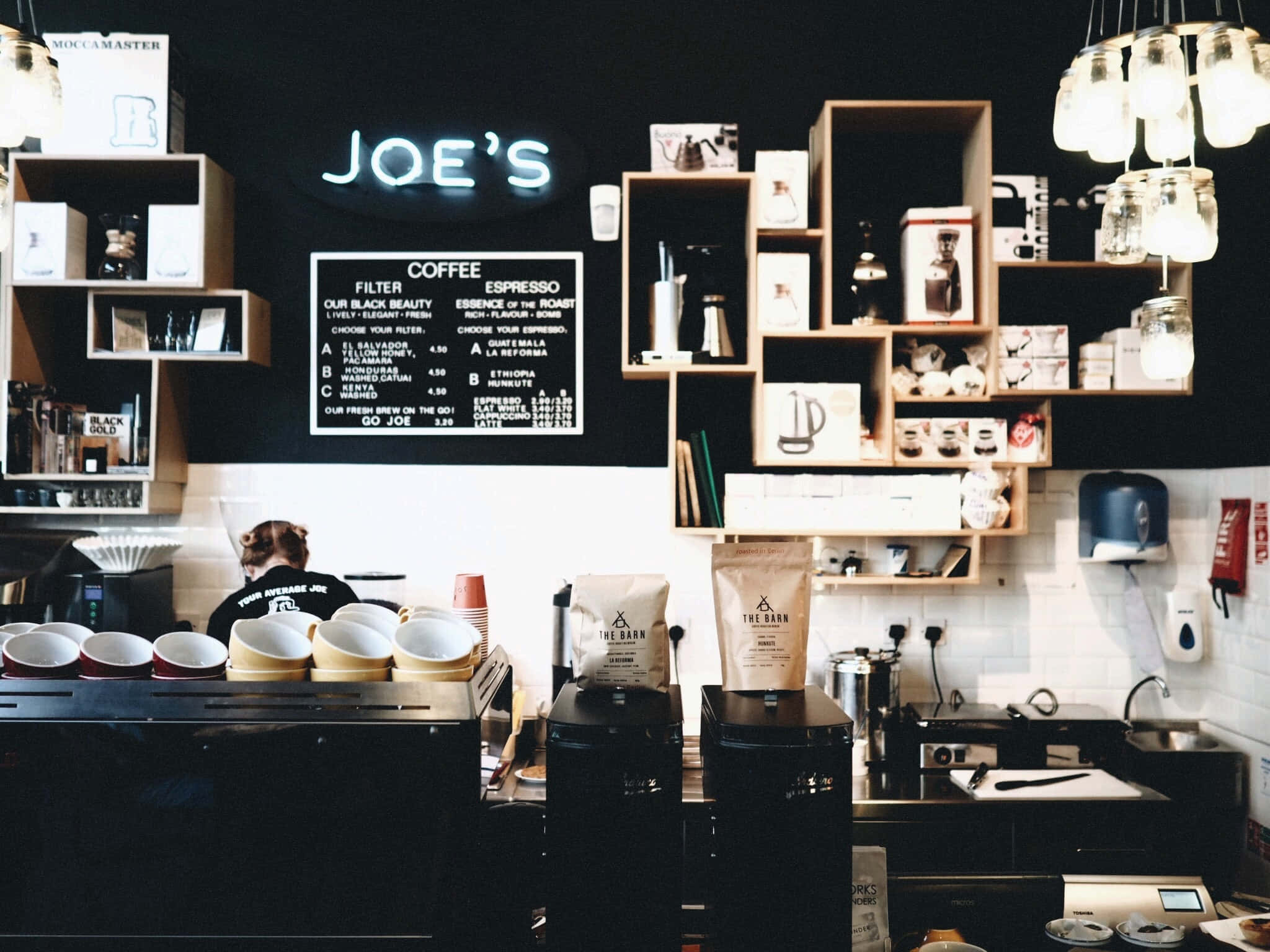 Coffee Aesthetic 桌布 壁紙 — 舒適的咖啡店內部，在發光的霓虹燈牌寫著Joe's下，咖啡師站在櫃檯後面。