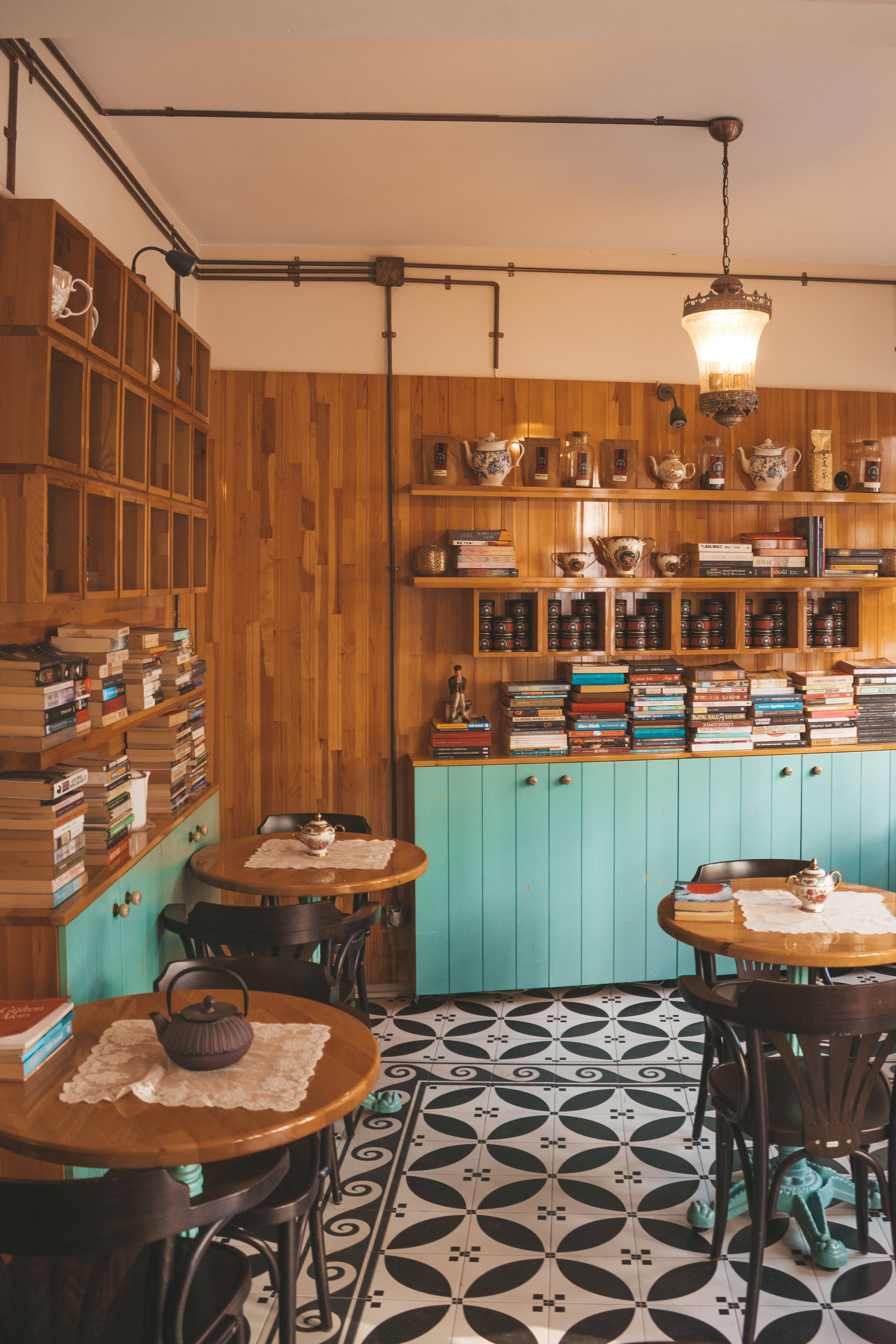 Coffee Shop 桌布 壁紙 — 舒適的咖啡館，配有堆滿書籍和茶壺的木架、藍綠色櫥櫃和黑白圖案地磚。