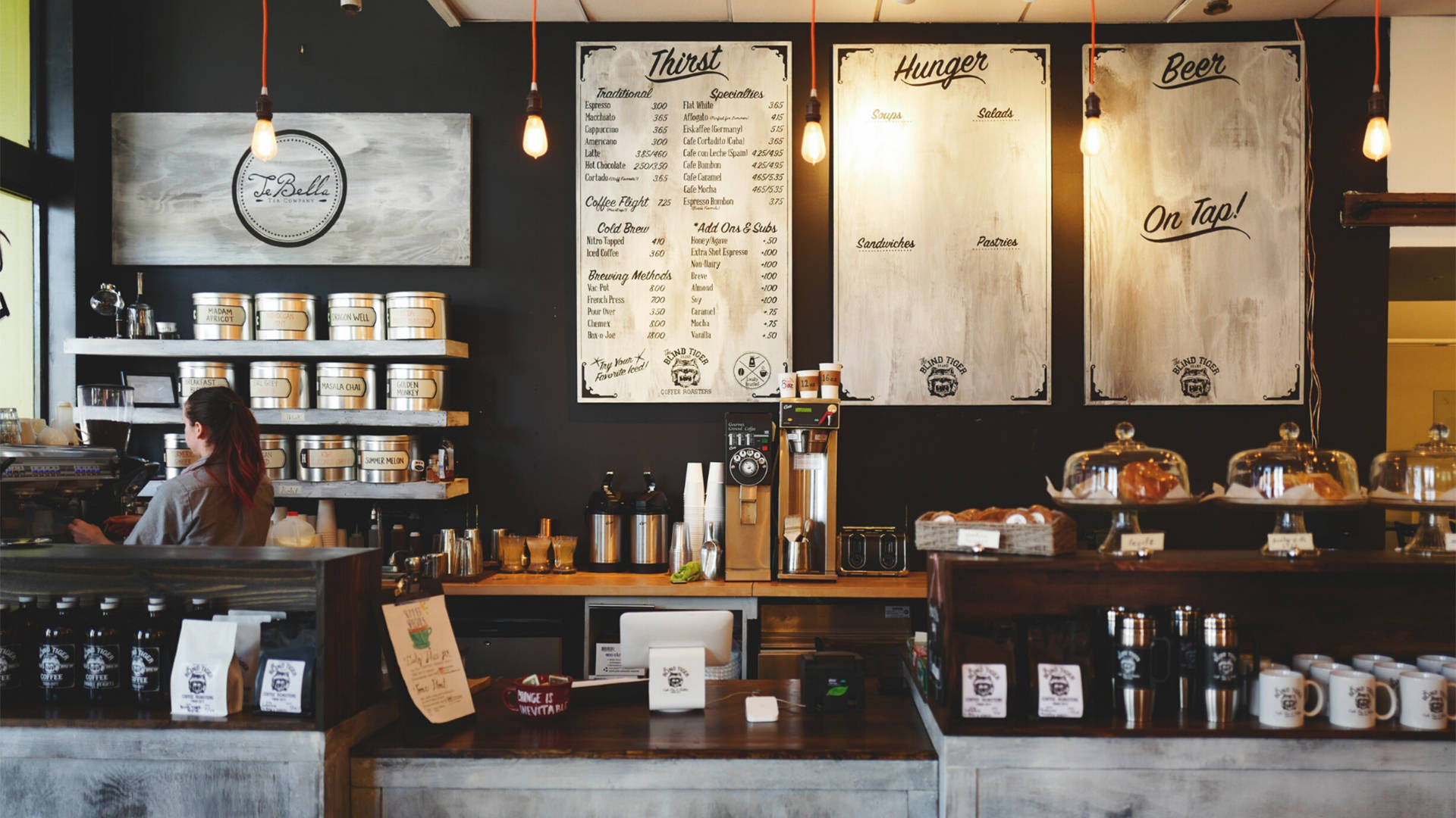 Coffee Shop 桌布 壁紙 — 舒適的咖啡館內部，咖啡師在櫃檯後面，鄉村風格的木質菜單，吊燈和咖啡豆架。