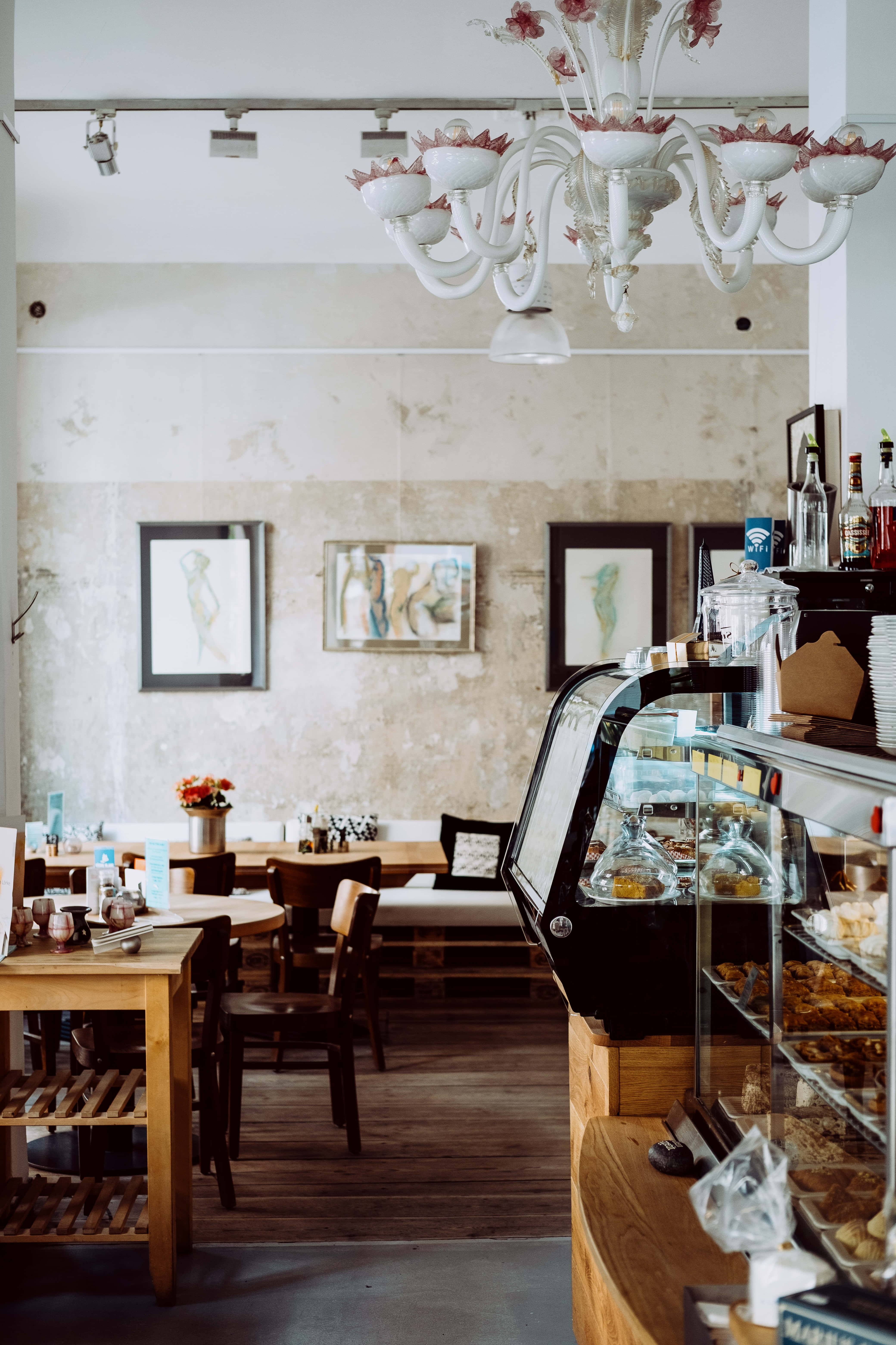Bakery 桌布 壁紙 — 舒適的咖啡館內部，設有木桌、椅子、裝滿糕點的玻璃展示櫃，以及頭頂上懸掛的華麗白色吊燈。