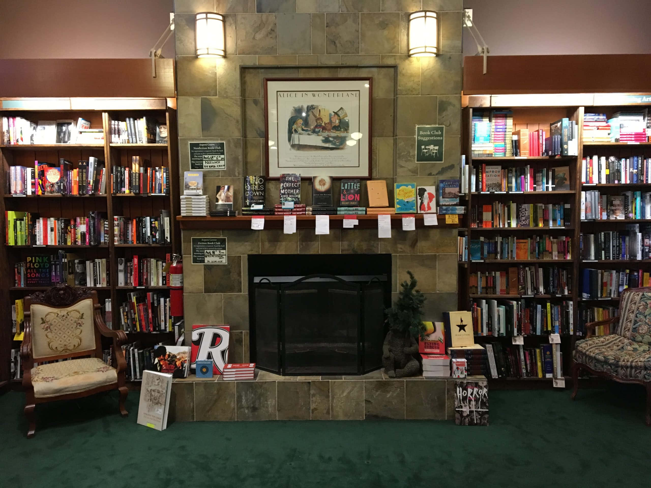 Bookshelf 桌布 壁紙 — 舒適的圖書館內部，設有石壁爐，兩旁是書架和復古扶手椅，在溫暖的燈光下。