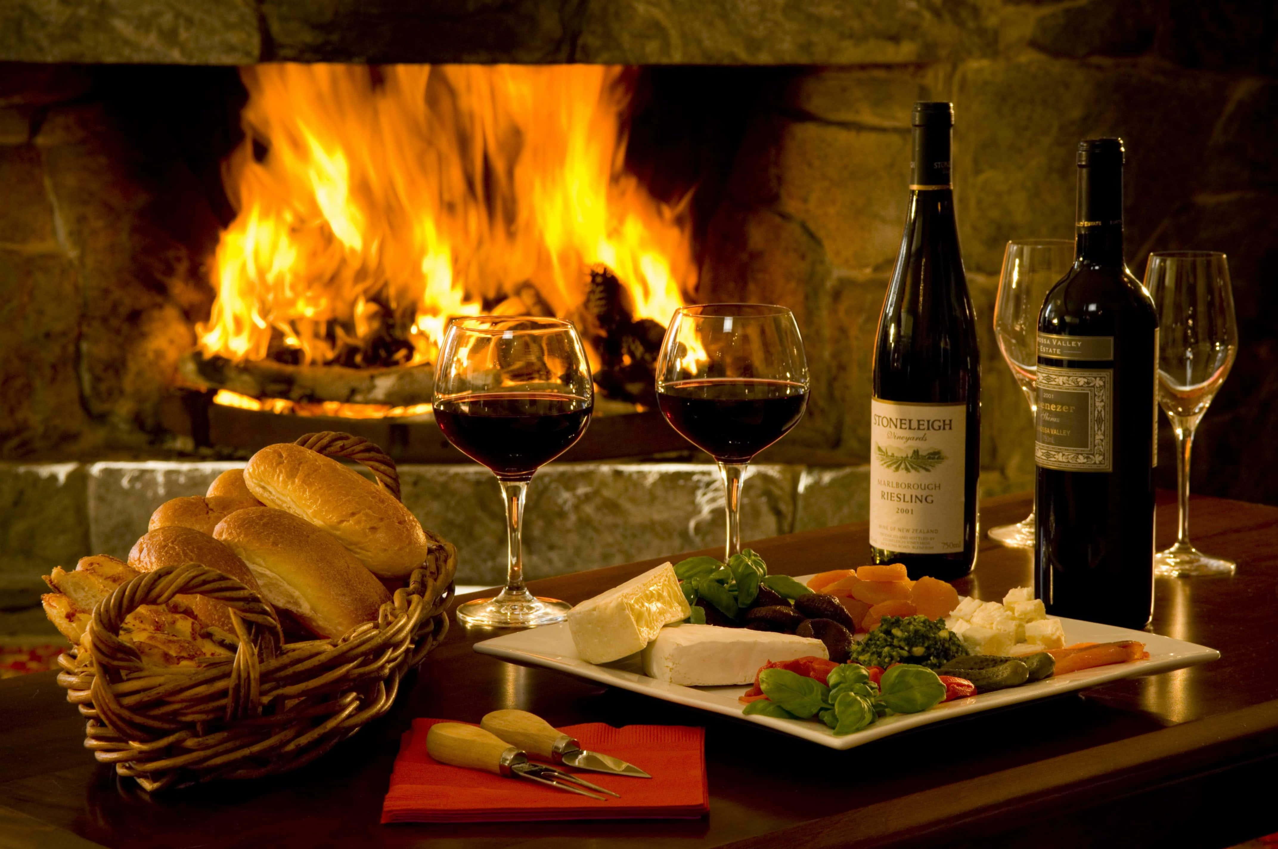 Autumn Fireplace 桌布 壁紙 — 舒適的壁爐光芒照亮了擺有酒瓶、酒杯、起司、麵包和新鮮香草的木桌。