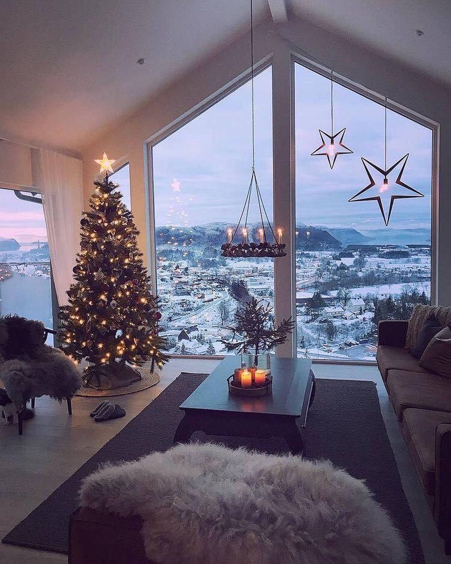 Cozy 桌布 壁紙 — 舒適的客廳，透過大窗戶可欣賞到黃昏時分點亮的聖誕樹和白雪覆蓋的山景。