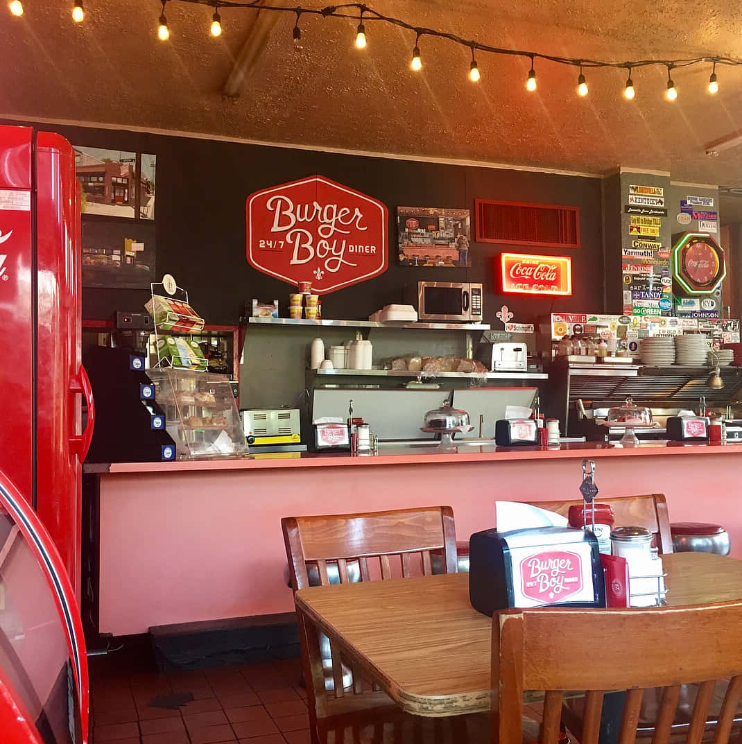 Restaurant 桌布 壁紙 — 舒適的復古餐廳，設有粉紅色牆壁、燈串、紅色冰箱、復古標誌和木桌。