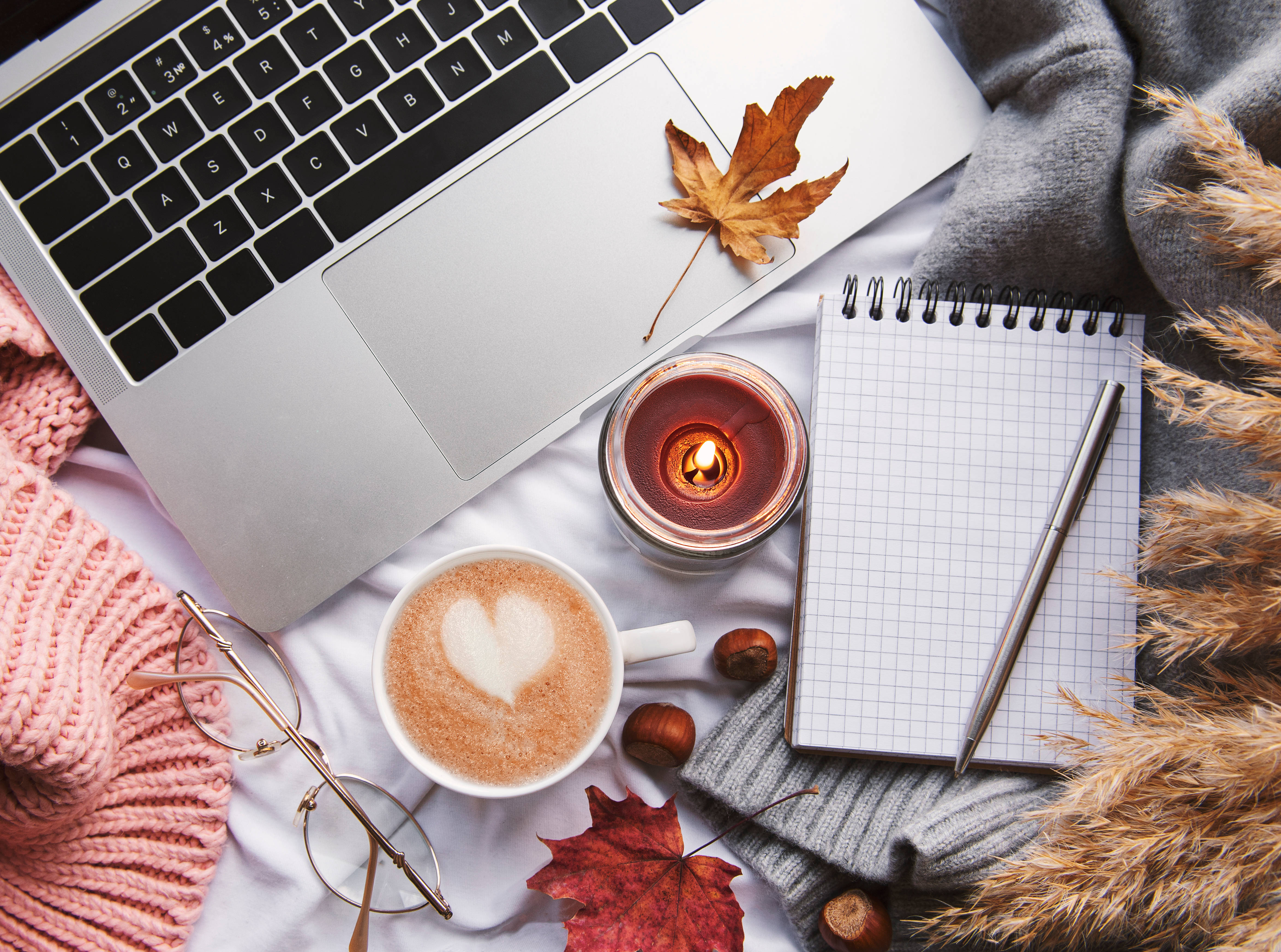 Autumn Season 桌布 壁紙 — 舒適的秋季工作空間，配有手提電腦、熱飲、蠟燭和筆記本，周圍環繞著落葉和針織品。