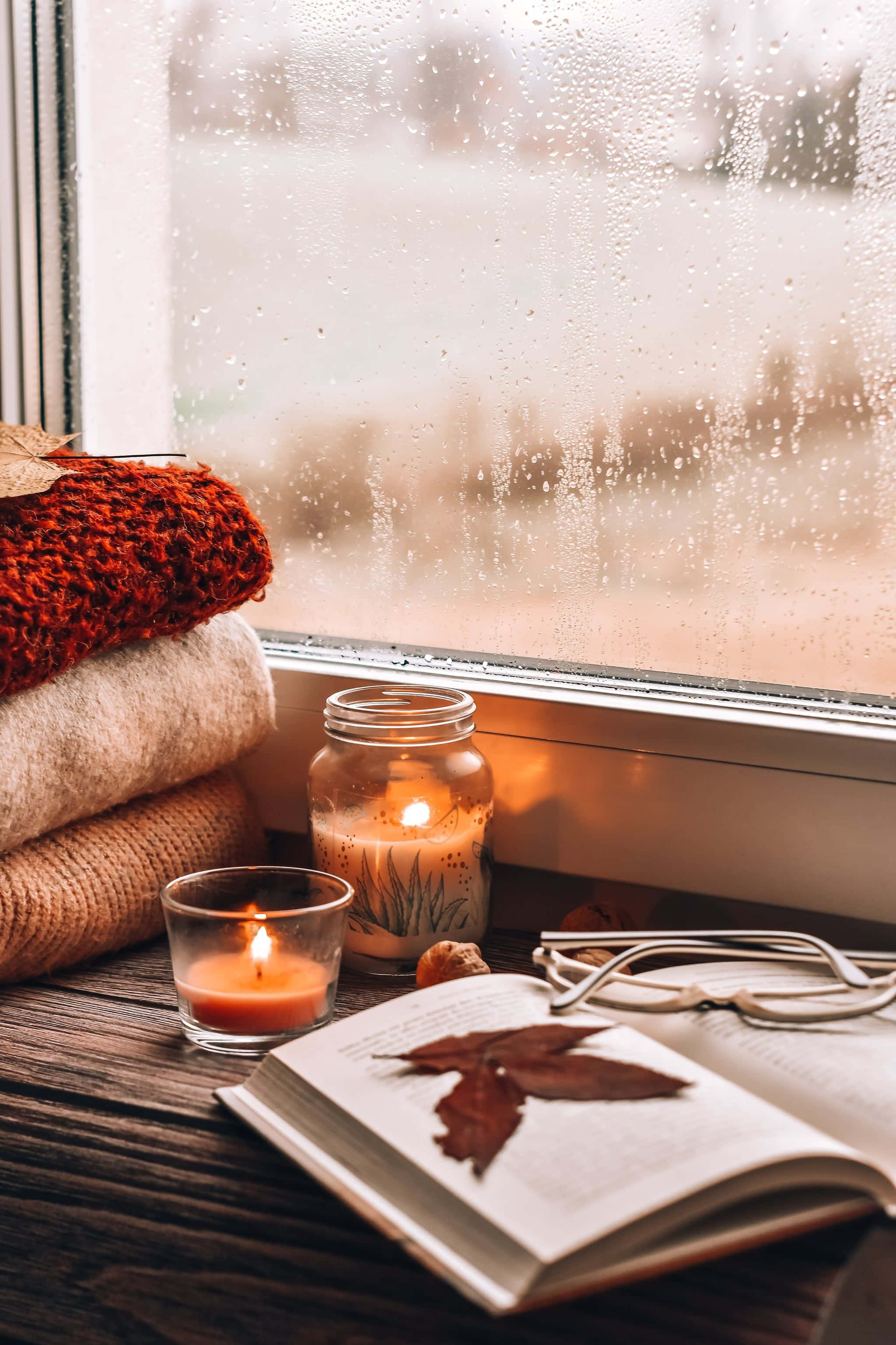 Cozy 桌布 壁紙 — 舒適的秋日場景，在雨天中，木製窗台上放著一本打開的書和針織毯子，旁邊有溫暖的蠟燭在發光。