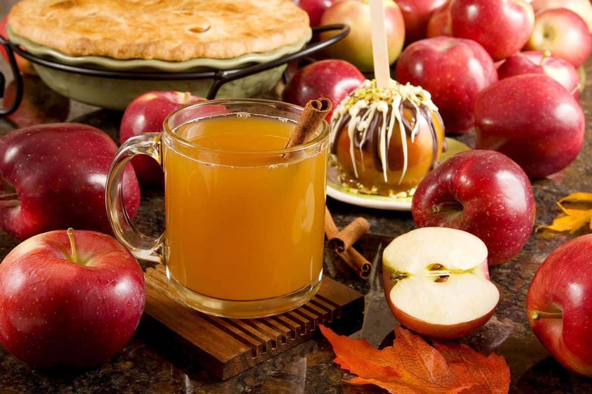 Fall Apples 桌布 壁紙 — 舒適的秋日靜物，展示一杯蘋果酒、焦糖蘋果、蘋果派和新鮮蘋果，周圍散落著落葉。