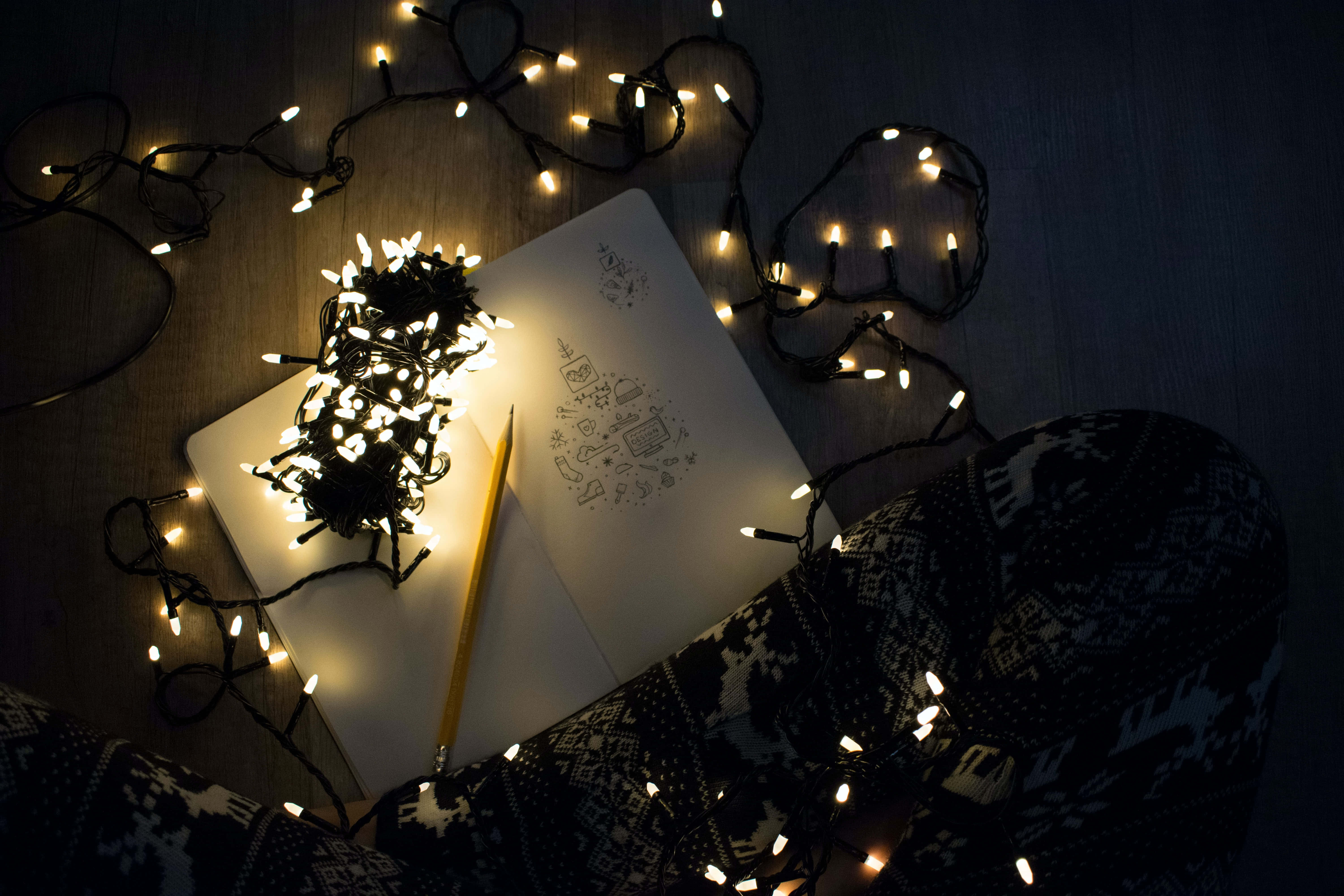 Christmas Light 桌布 壁紙 — 舒適的筆記本和鉛筆在木地板上被燈串溫暖地照亮，旁邊是圖案睡衣。